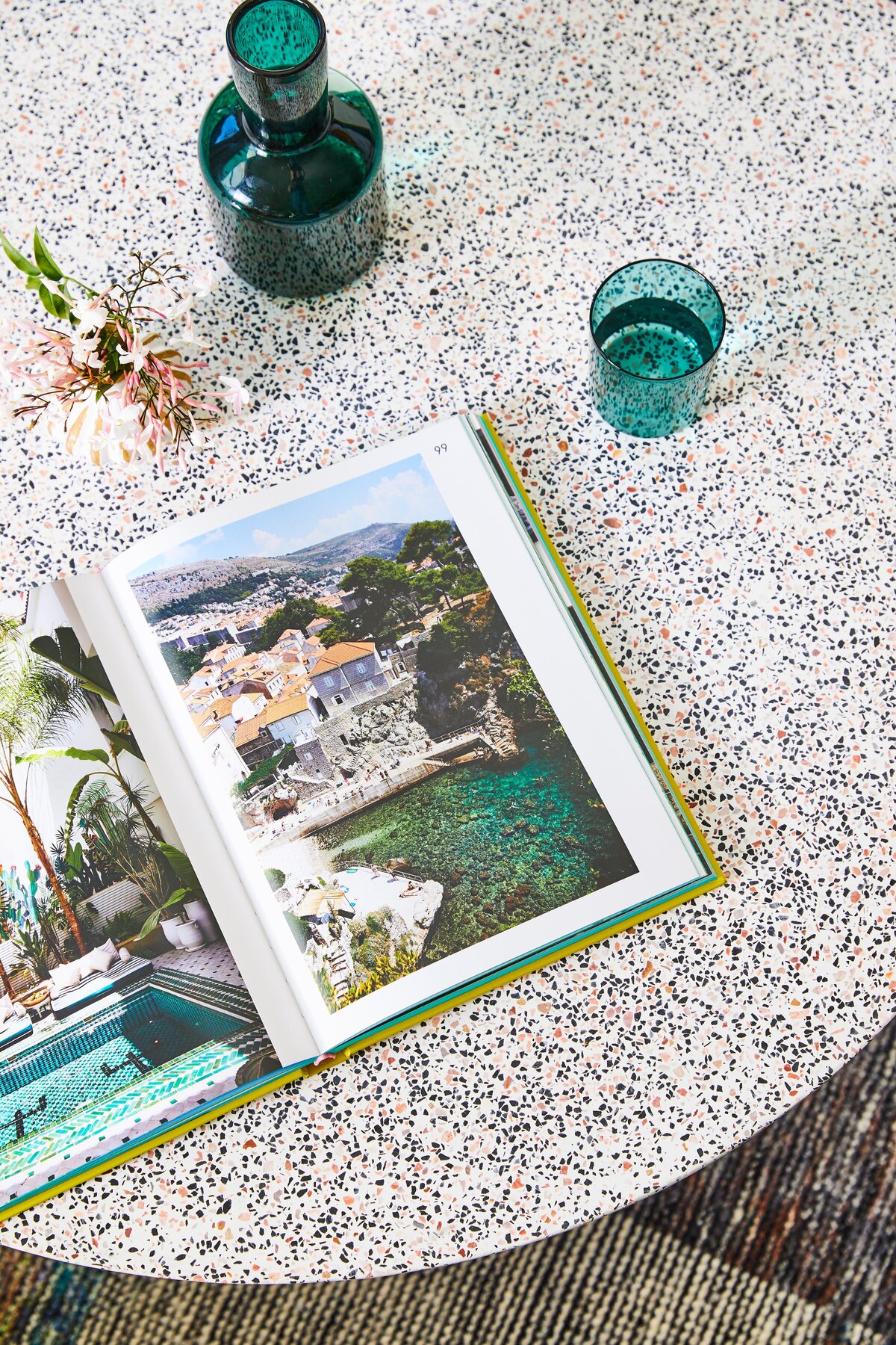 Terrazzo coffee table styled with green glassware and open travel book in Elwood apartment living room