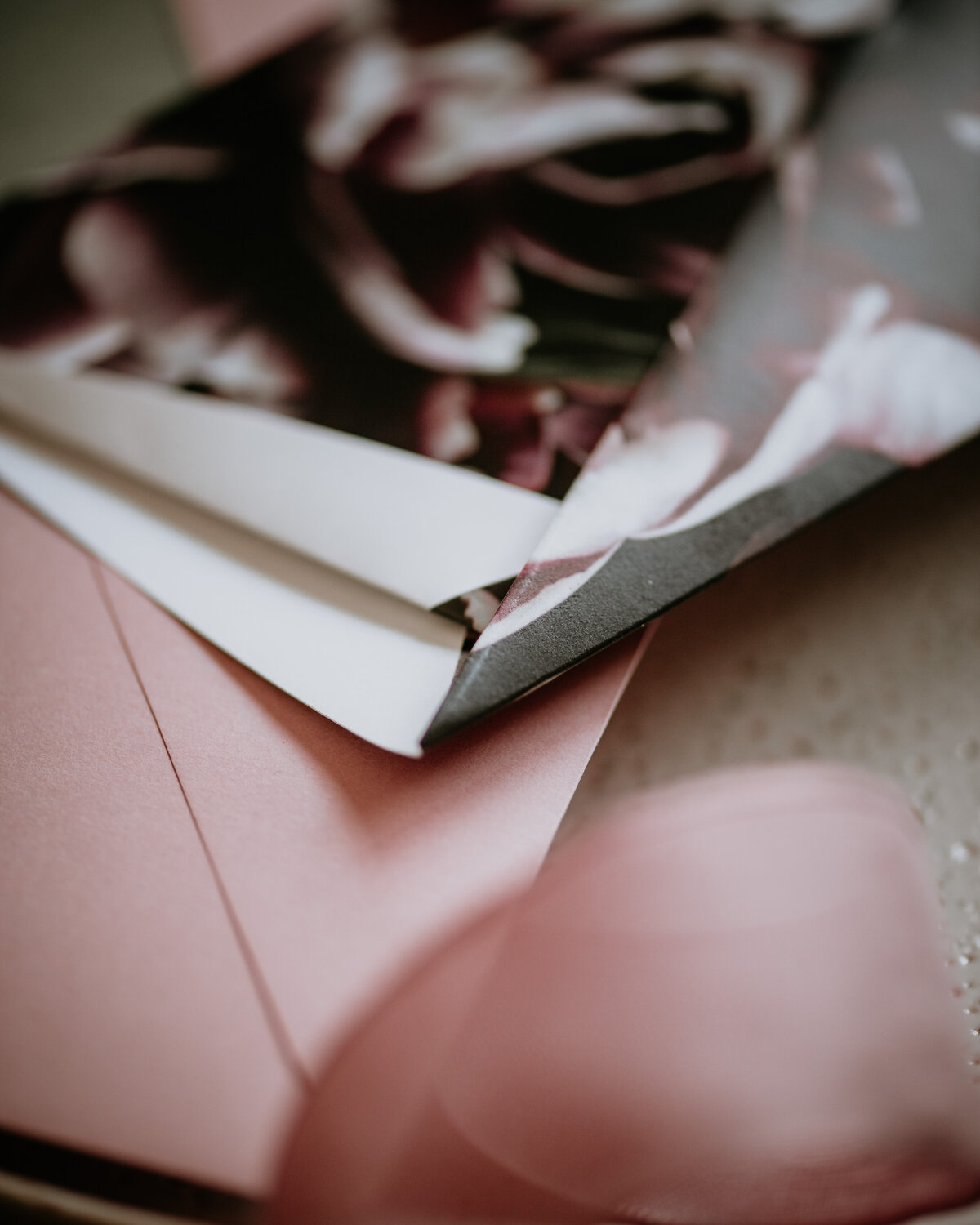 Close up of folded origami wedding invitation and pink florals
