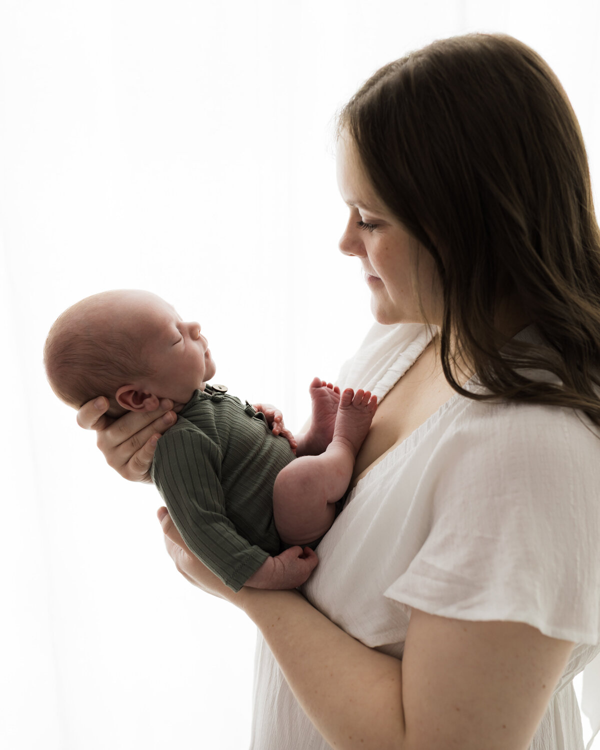 mom in white dress holding newborn baby boy in green onesie