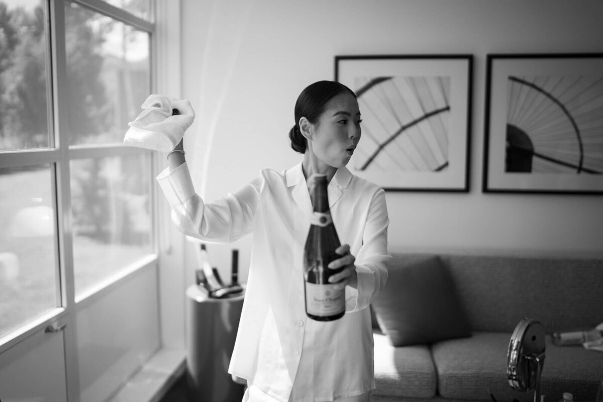 Bride pops a bottle of champagne while getting ready for her Aspen Meadows Resort wedding ceremony.