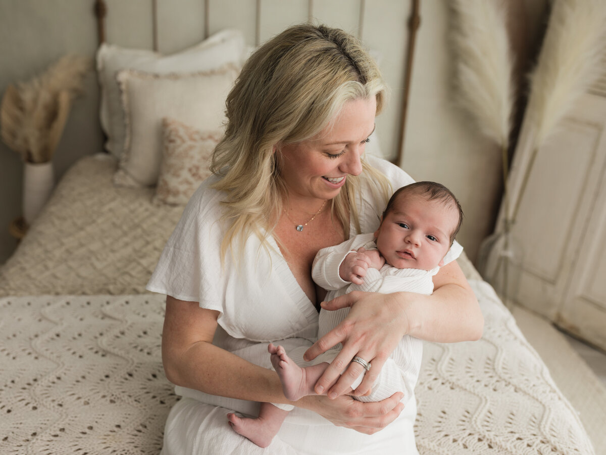 mom holding newborn baby boy in white onesie for studio lifestyle session cleveland newborn photographer