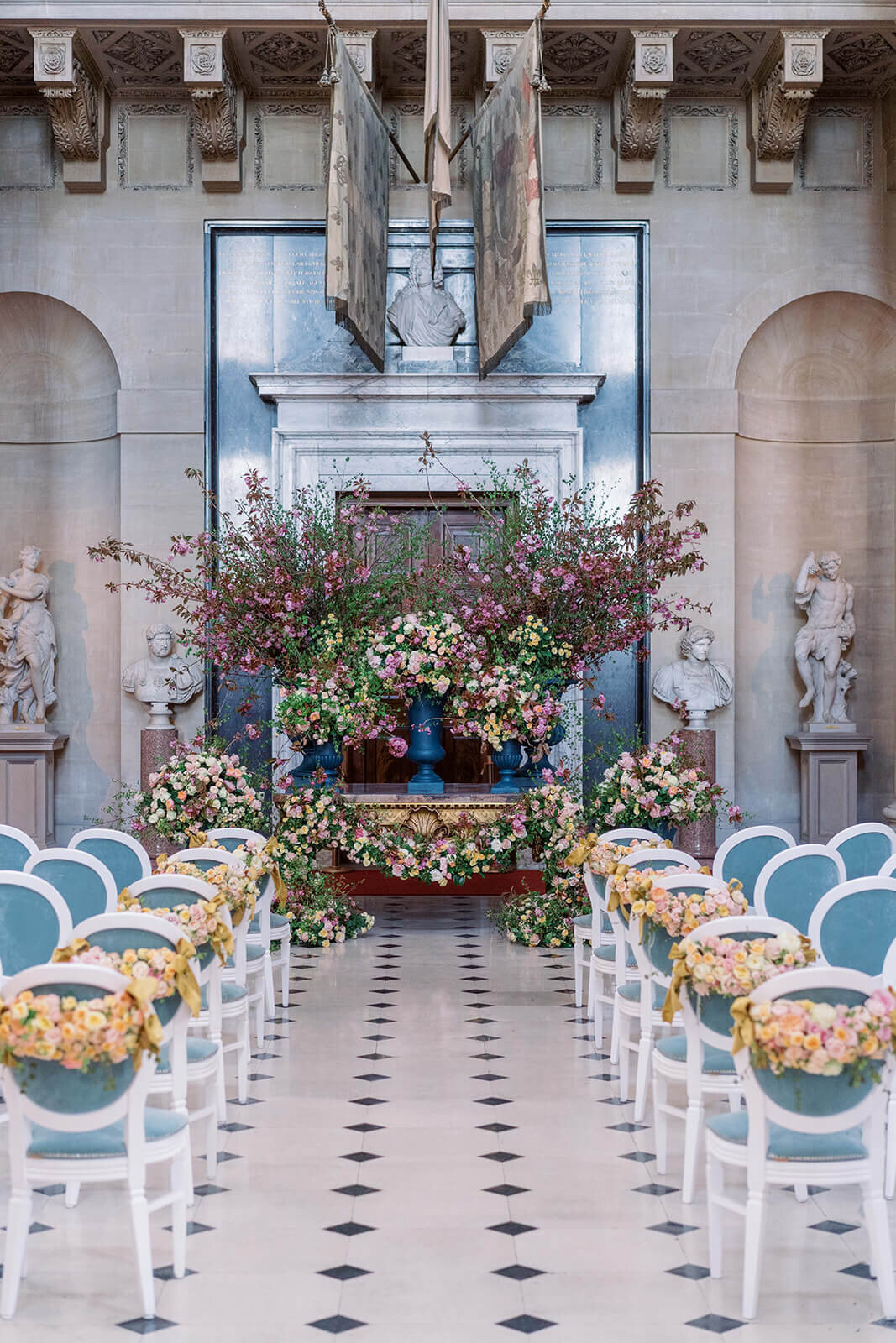 view down a wedding ceremony aisle at blenheim palace with rows of teal chairs which have peach flower swags on the back of them