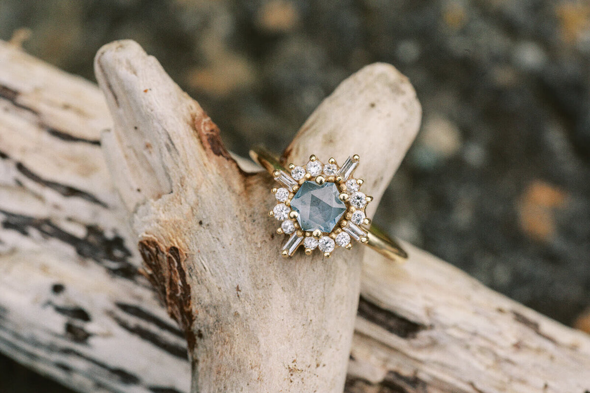 An engagement ring with a blue stone on a piece of driftwood. 