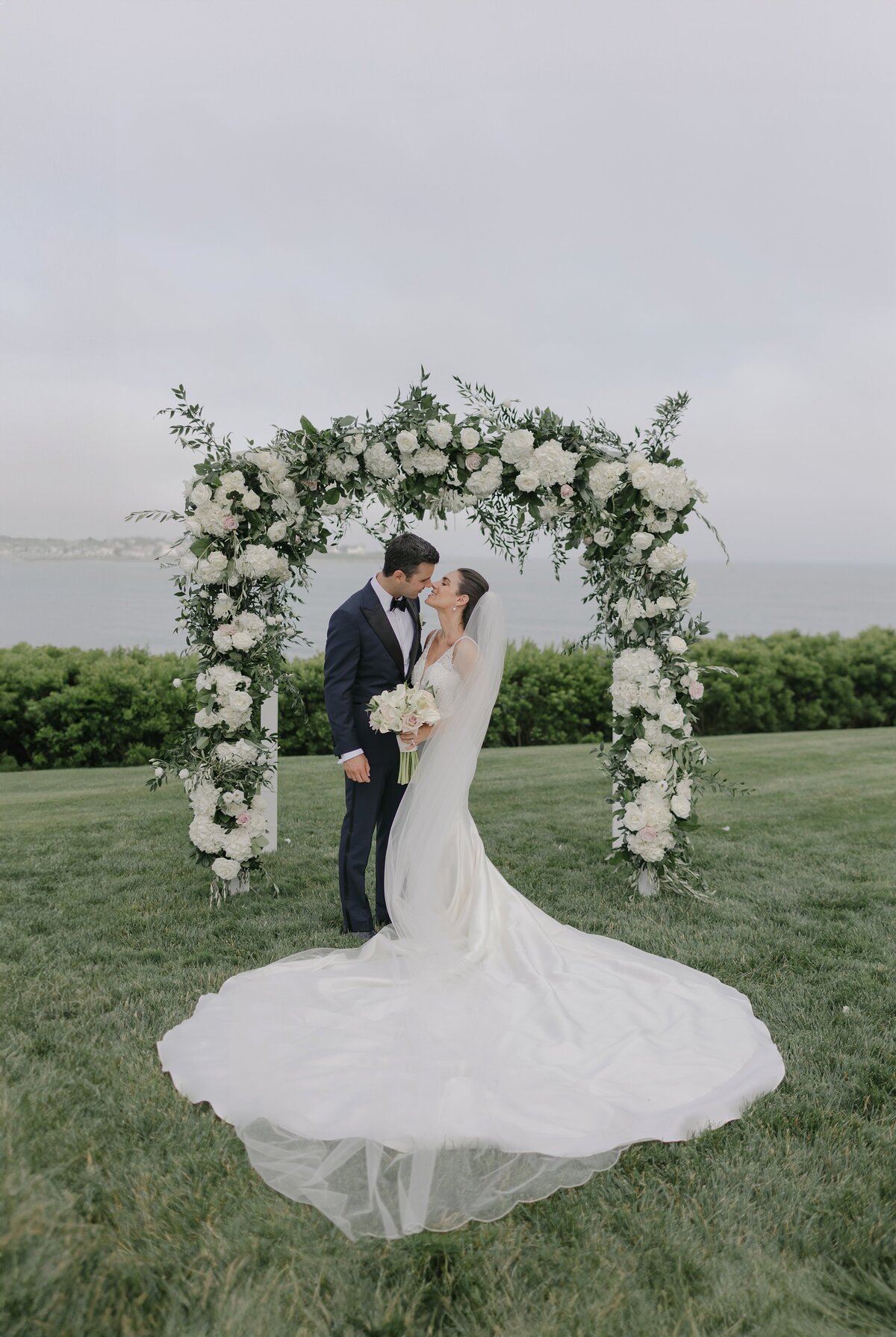 Bride and Groom kiss under floral arbor overlooking ocean during wedding at The Chanler, Newport.