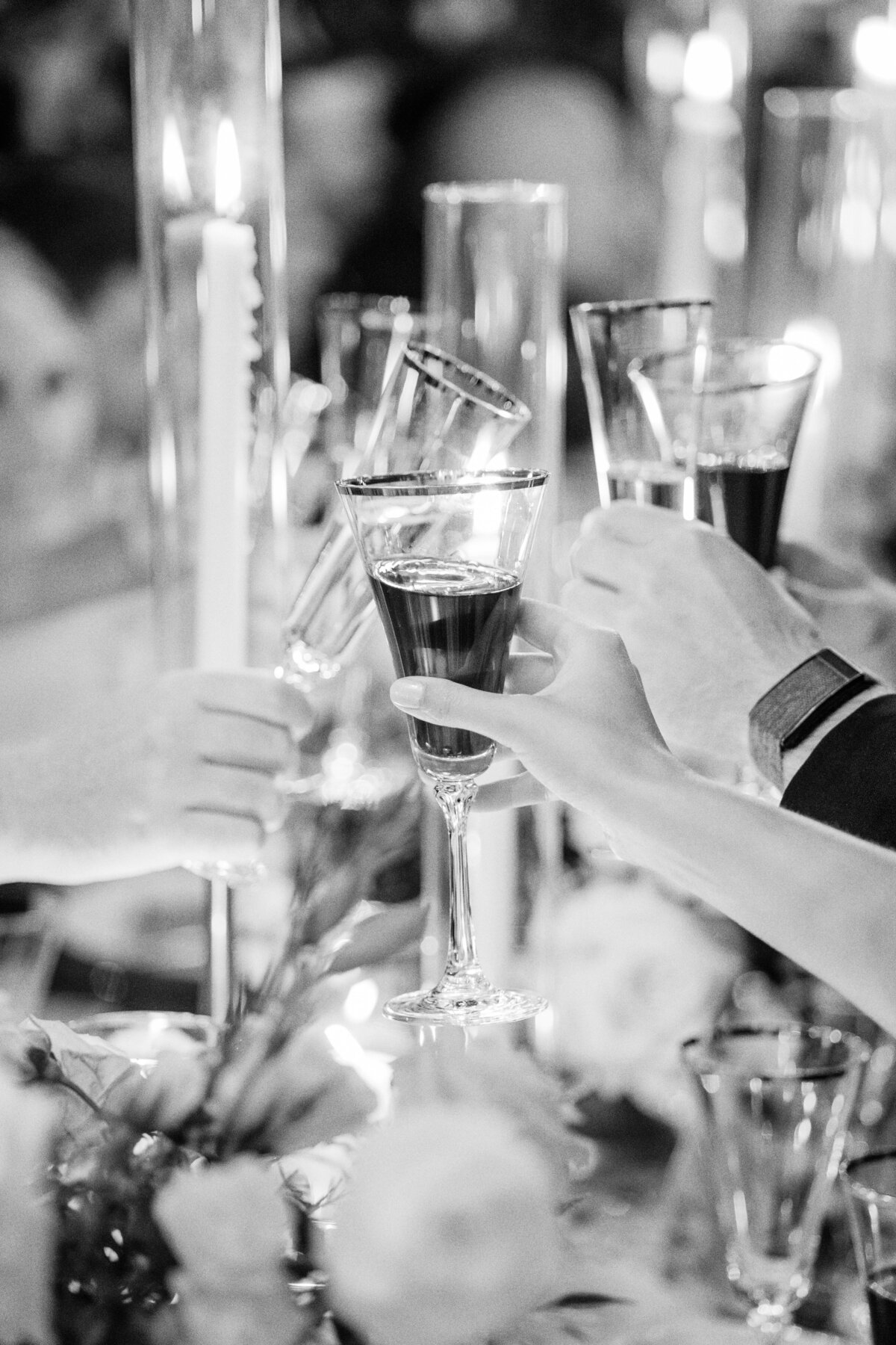 A heartfelt wedding toast captured in a black and white image, with guests raising their glasses in a candlelit reception setting.
