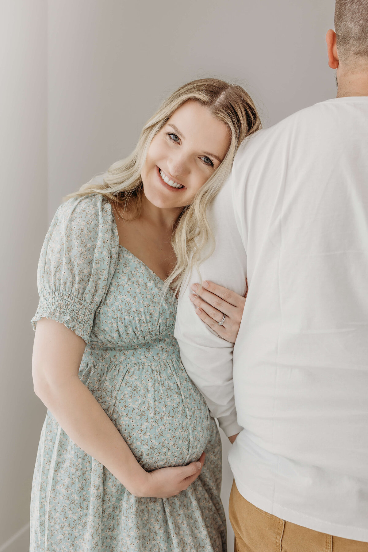 Expecting mom holding husband's arm and smiling for camera