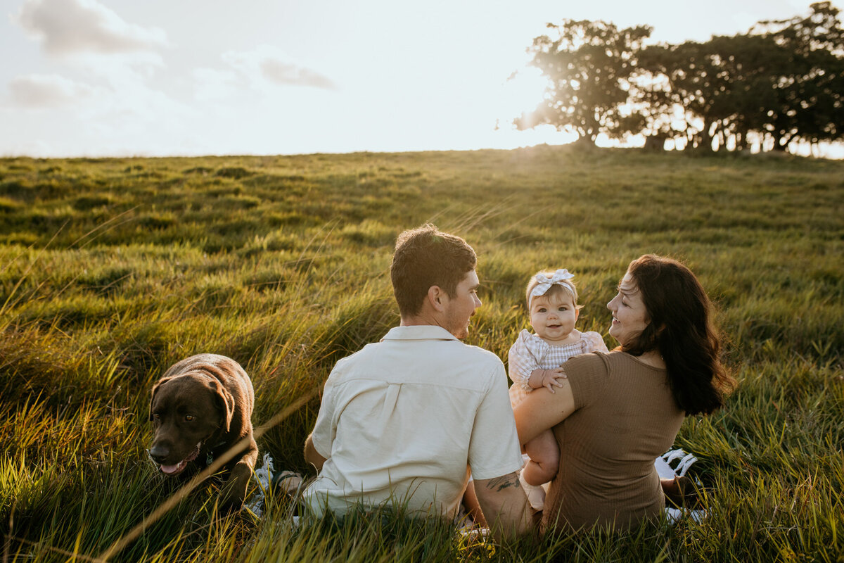 Cute moment of a family sitting on a grass field with a brown Labrador. 
