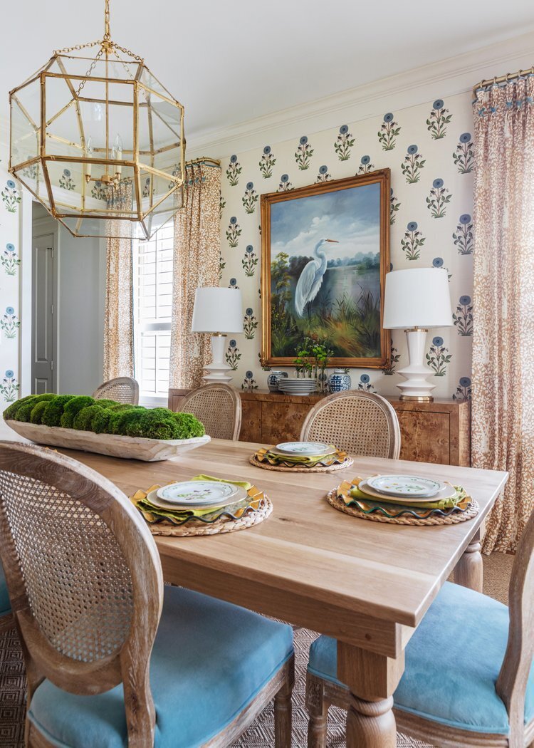 oyster creek studios oak forest remodel blue cushioned chairs around a wooden dining roo table with gold lighting and heron painting