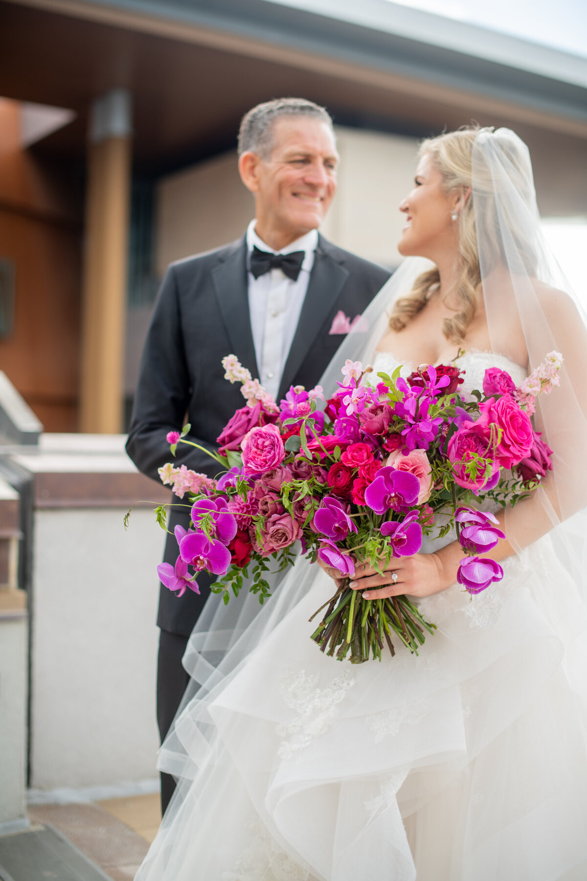 Eye-catching bright pink and fuchsia bridal bouquet composed of phalaenopsis and makara orchids, peonies, garden roses, and ranunculus. Design by Rosemary and Finch in Nashville, TN.