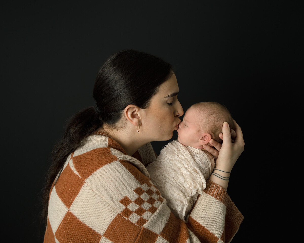 Mom holding her newborn baby girl giving her a kiss.