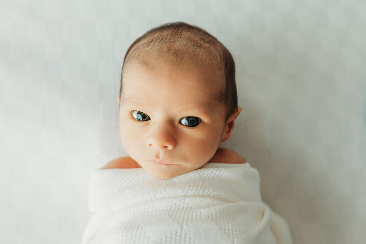 baby boy wide awake swaddled in white for his newborn portraits in york