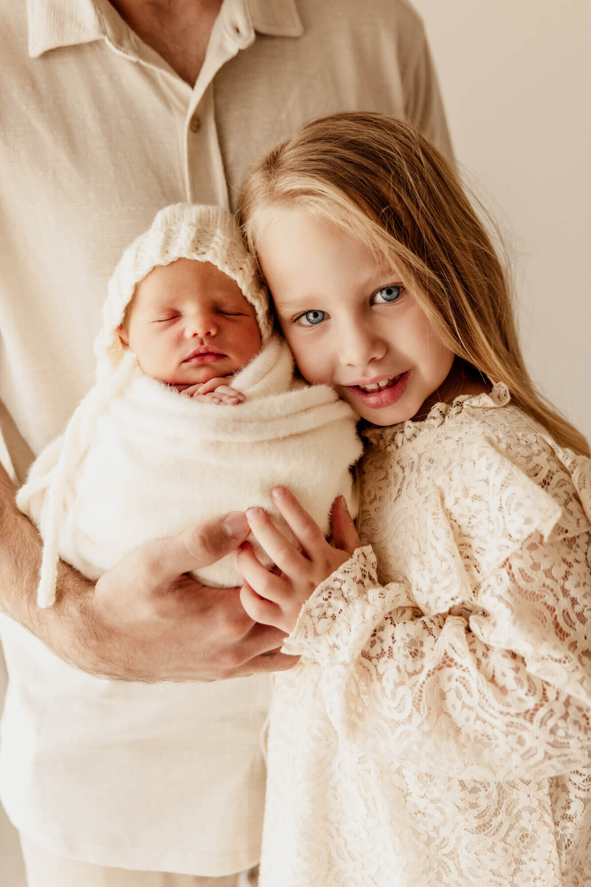 Girl with blonde hair and blue eyes with her face near her swaddled sister's head.