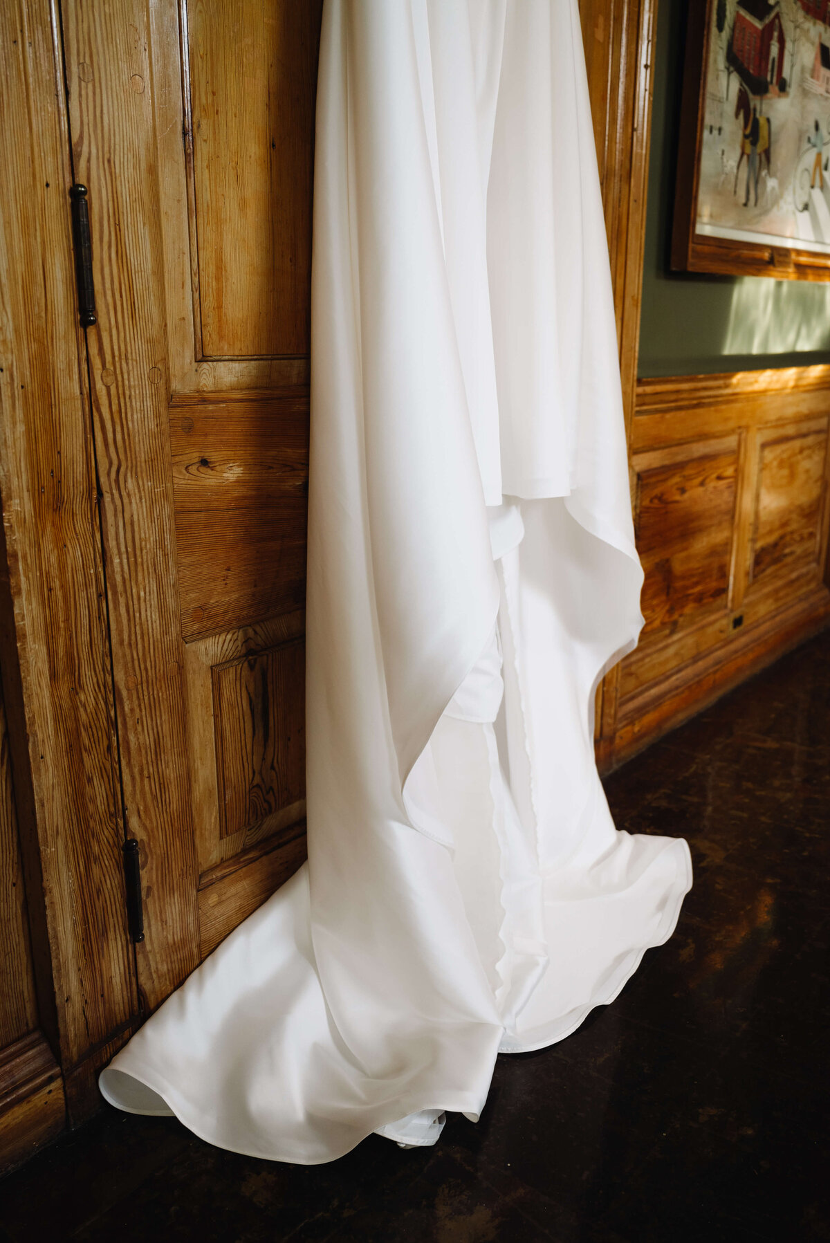 detail shot of wedding dress train laying on the floor as the gown hangs on the edge of the wooden door