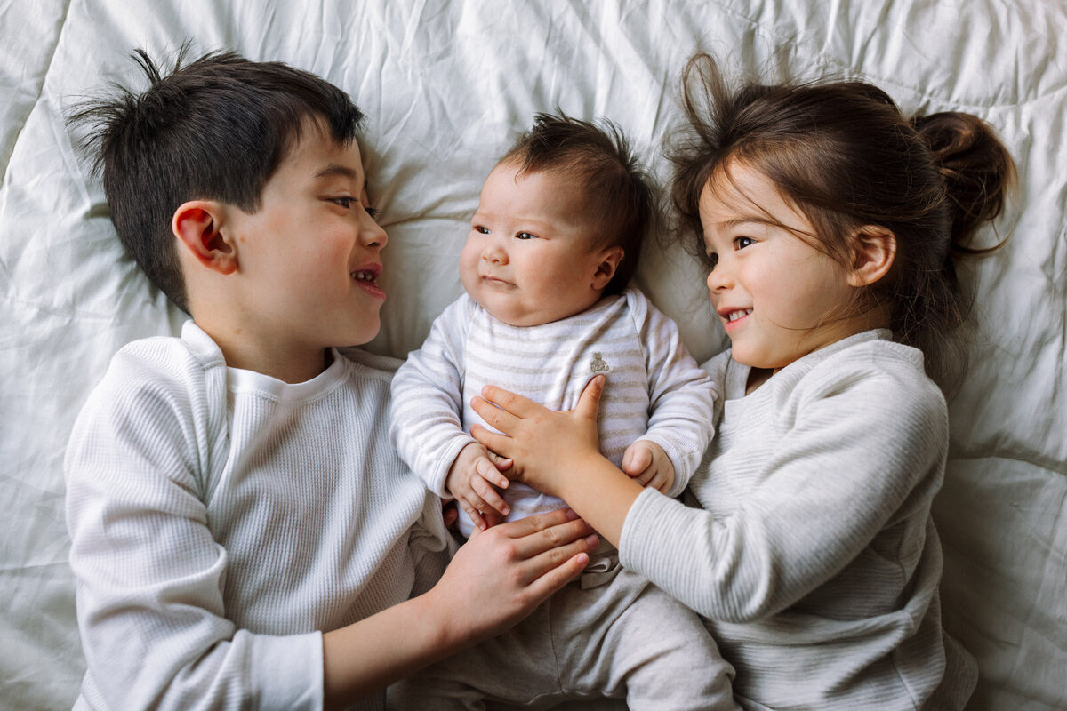 two brothers snuggling on either side of baby sister all wearing neutral colors