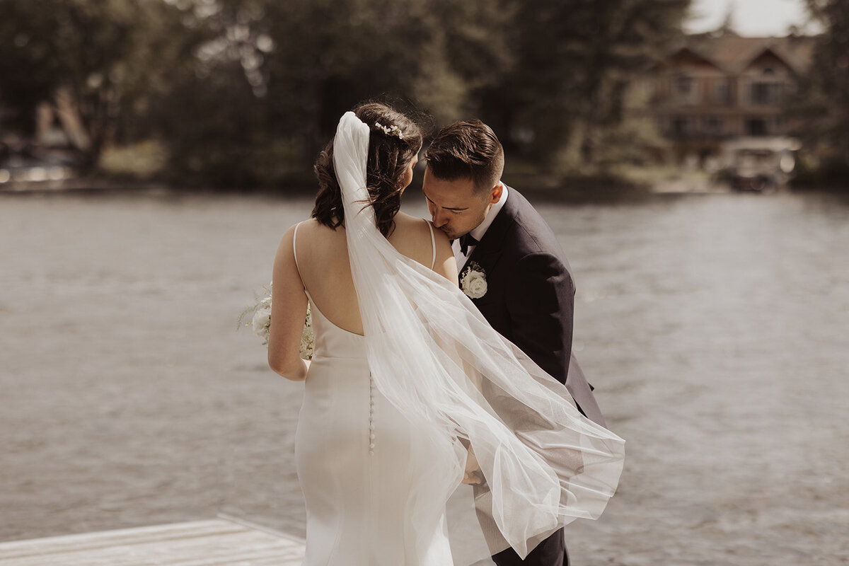 A couple embracing by a river with the bride’s veil flowing.