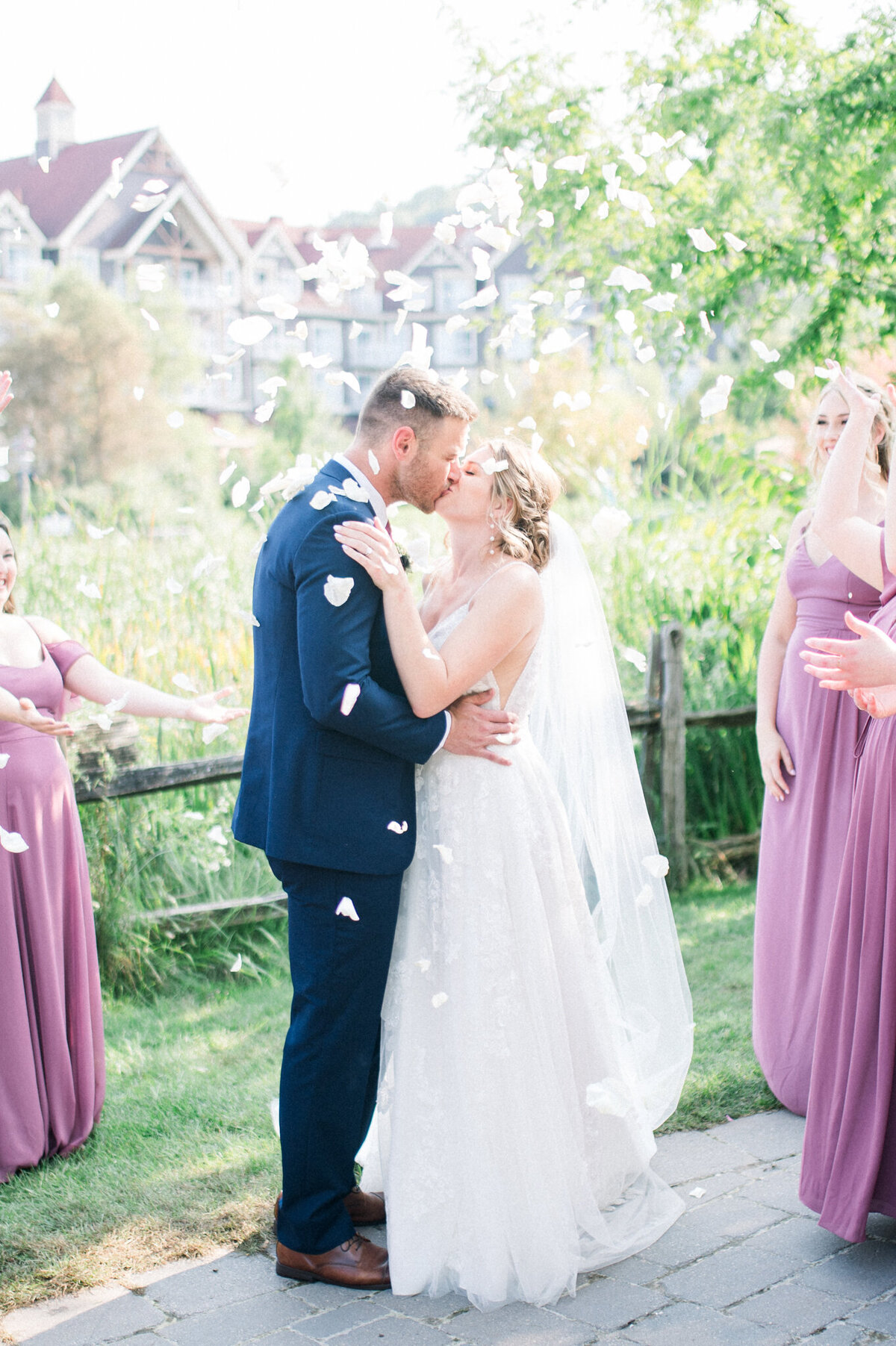 Bride and groom kiss while wedding party throws flower pedals over them captured by Niagara wedding photographer
