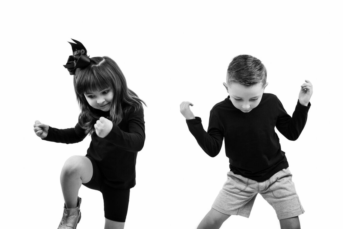 High-key, high-contrast candid studio portrait of two children dancing joyfully, captured in a bright and playful setting.