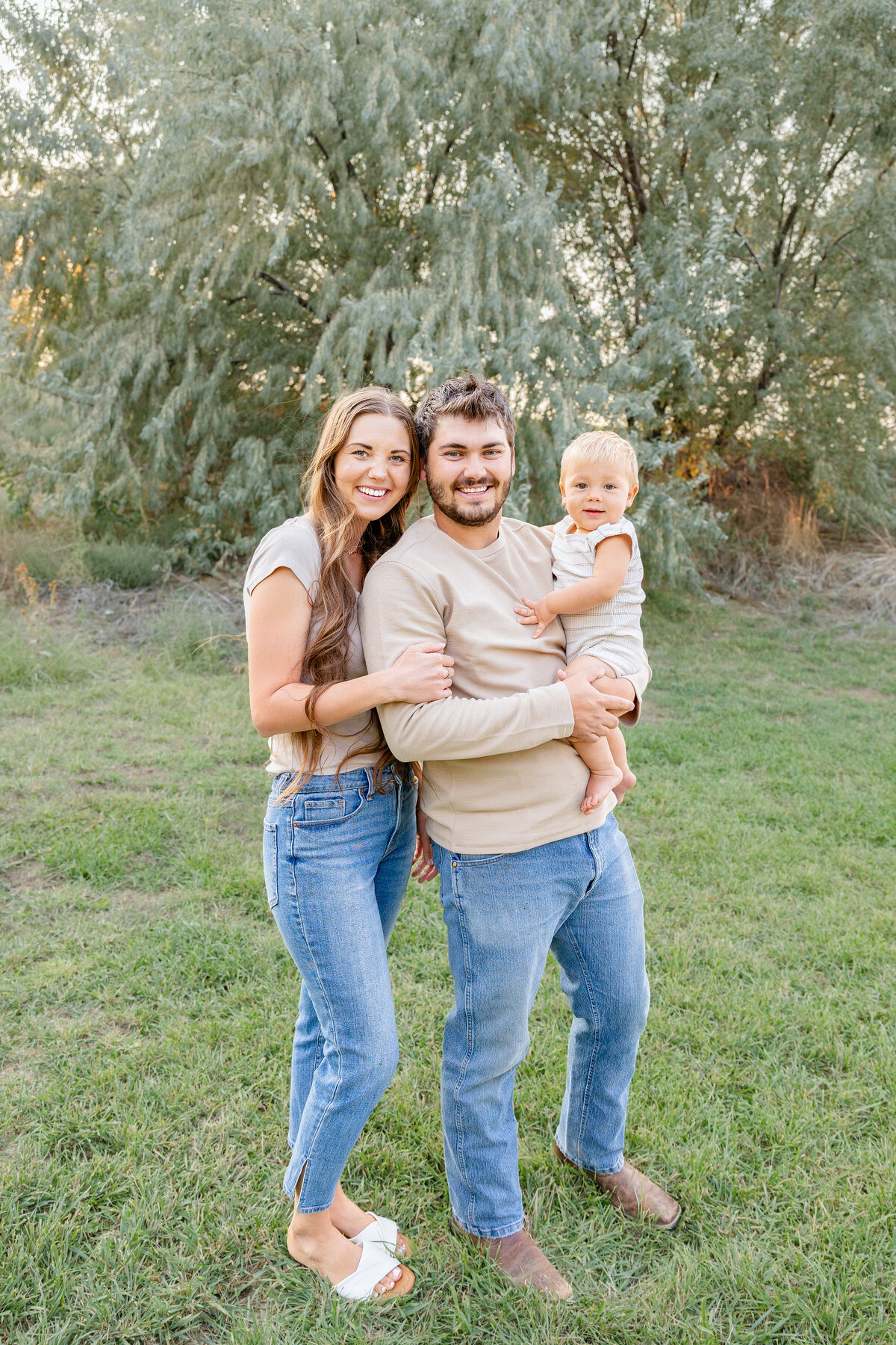 A beautiful family smiling together in a natural setting, holding their baby boy in their arms, captured by Cassie Lee Photography.
