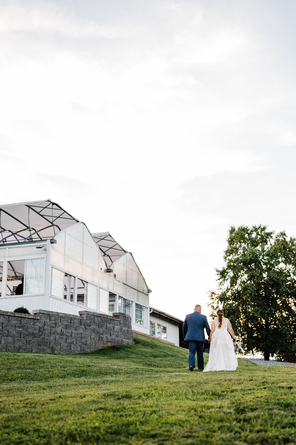 showalter's orchard and greenhouse wedding with bride and groom holding hands and walking up a hill together towards the greenhouse at sunset