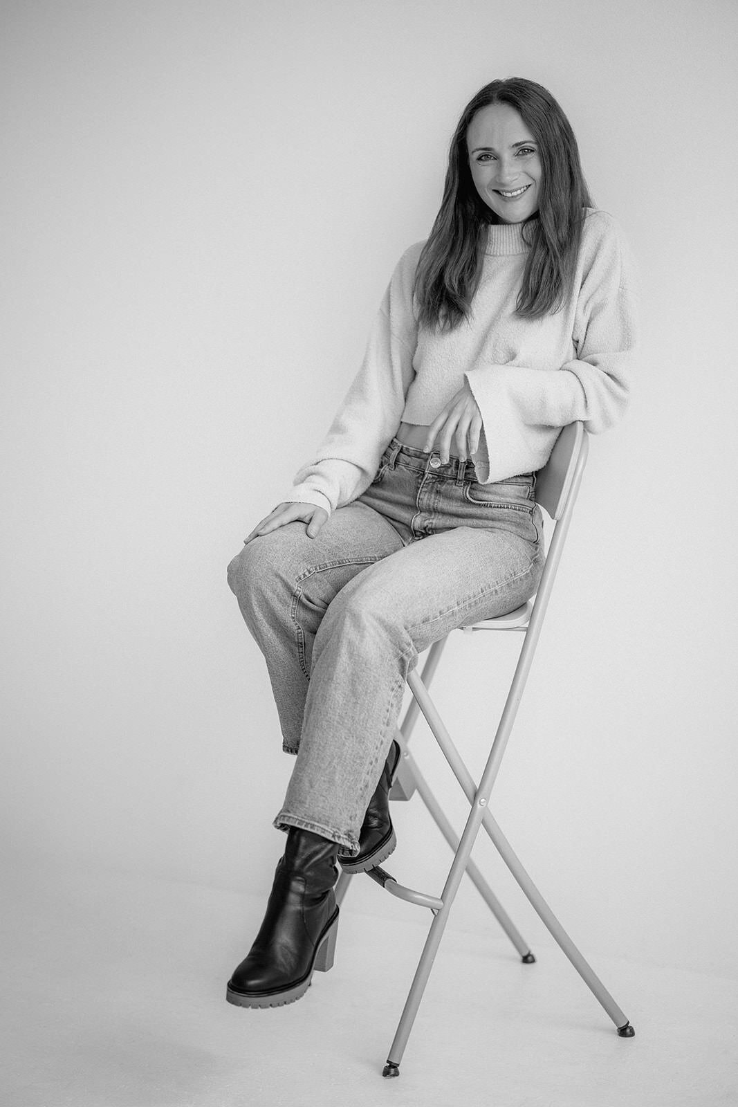 Woman sitting on a high chair and leaning onto the back of the chair.