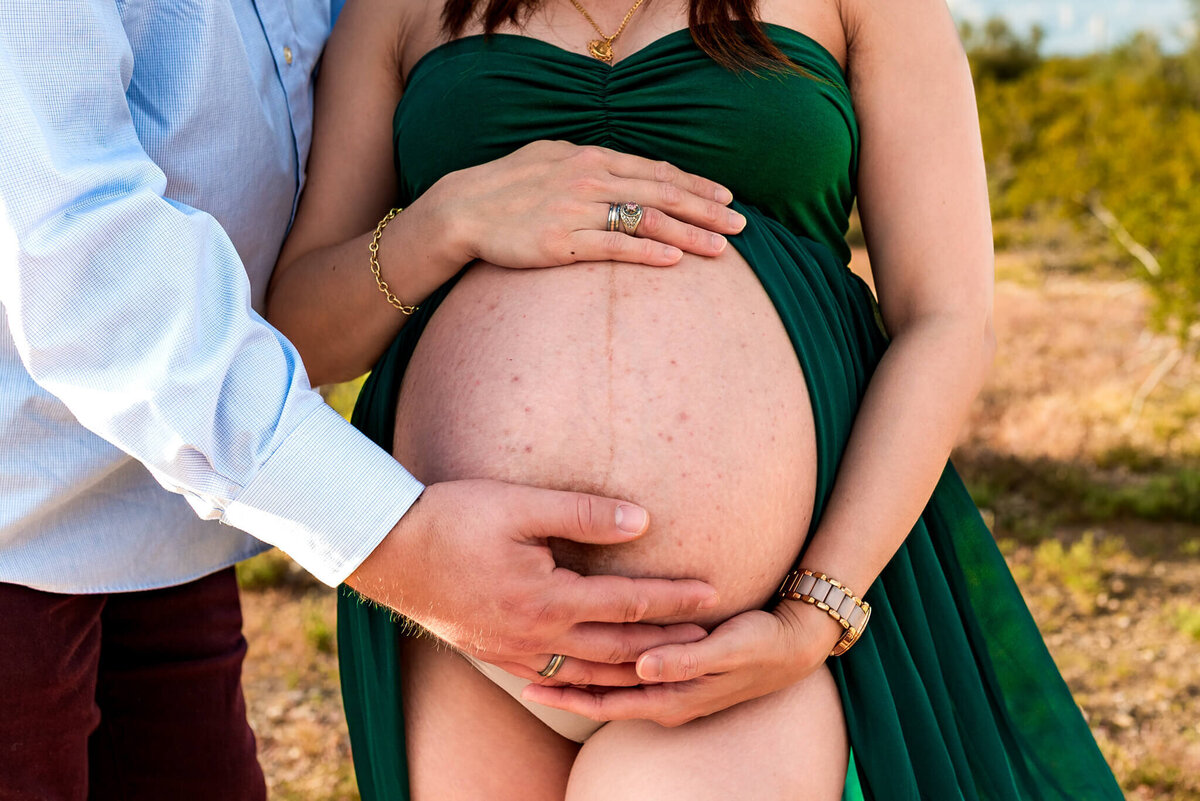 Close up photo of expecting mother's belly, surrounded by her and her husband's hands
