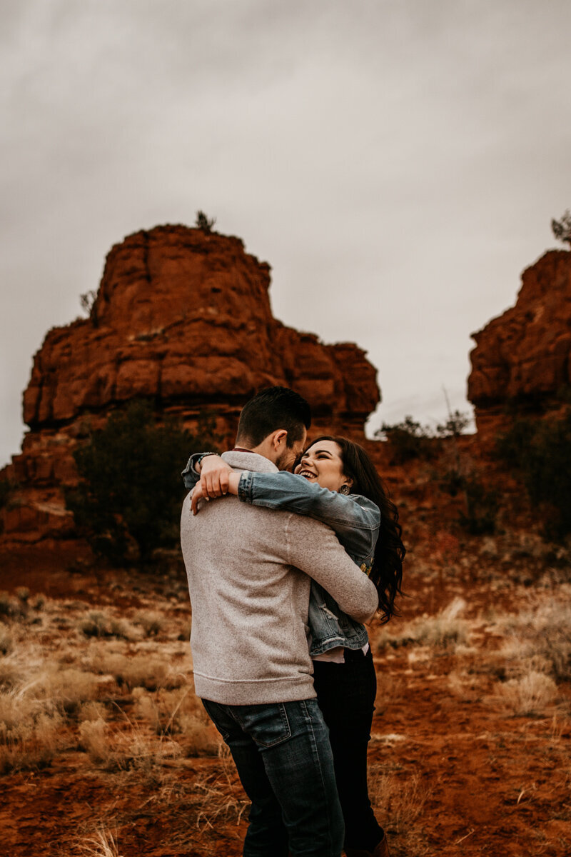 man holding and spinning fiancé in front of red rocks