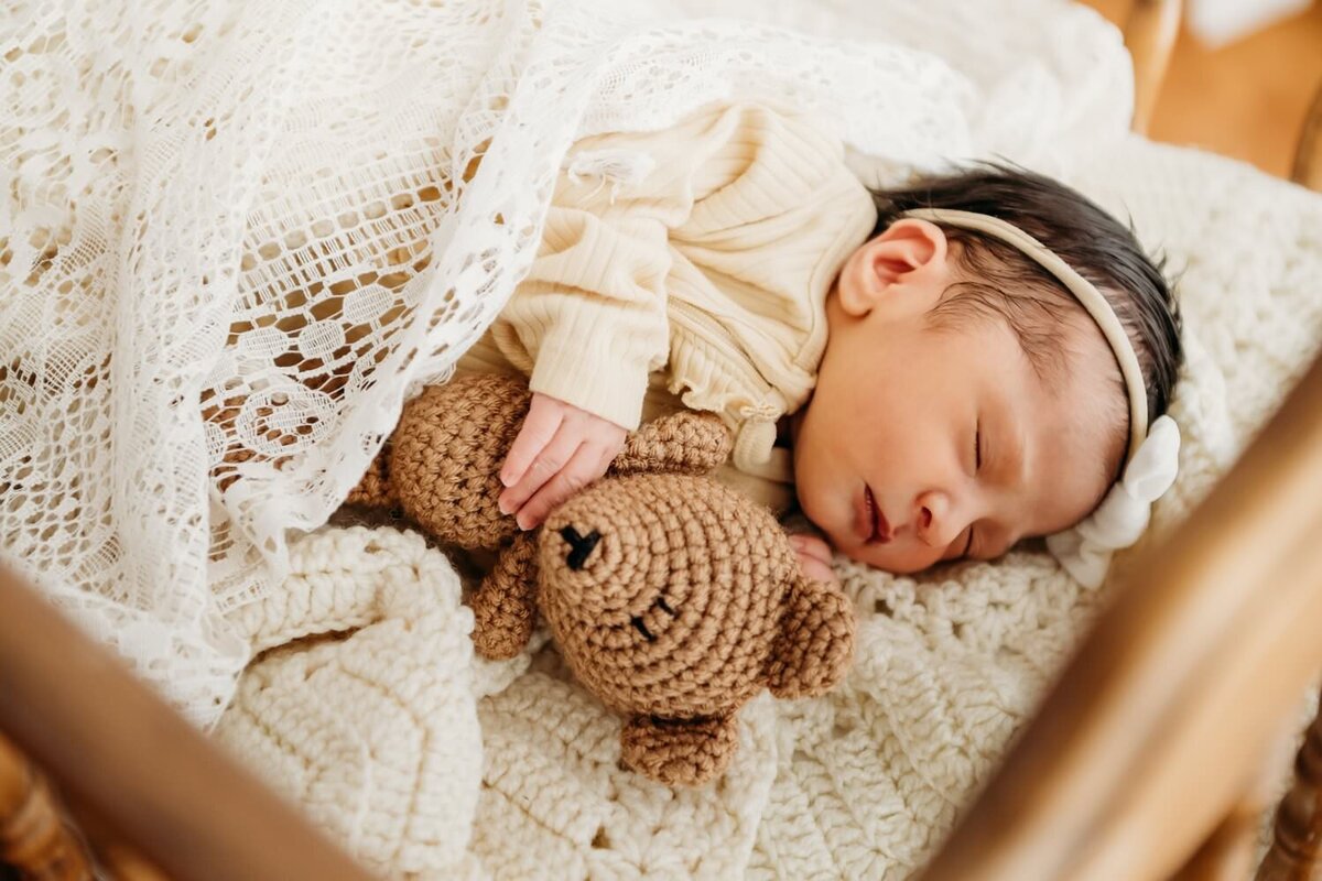 baby in vintage wooden crib with crocheted bear next to her.