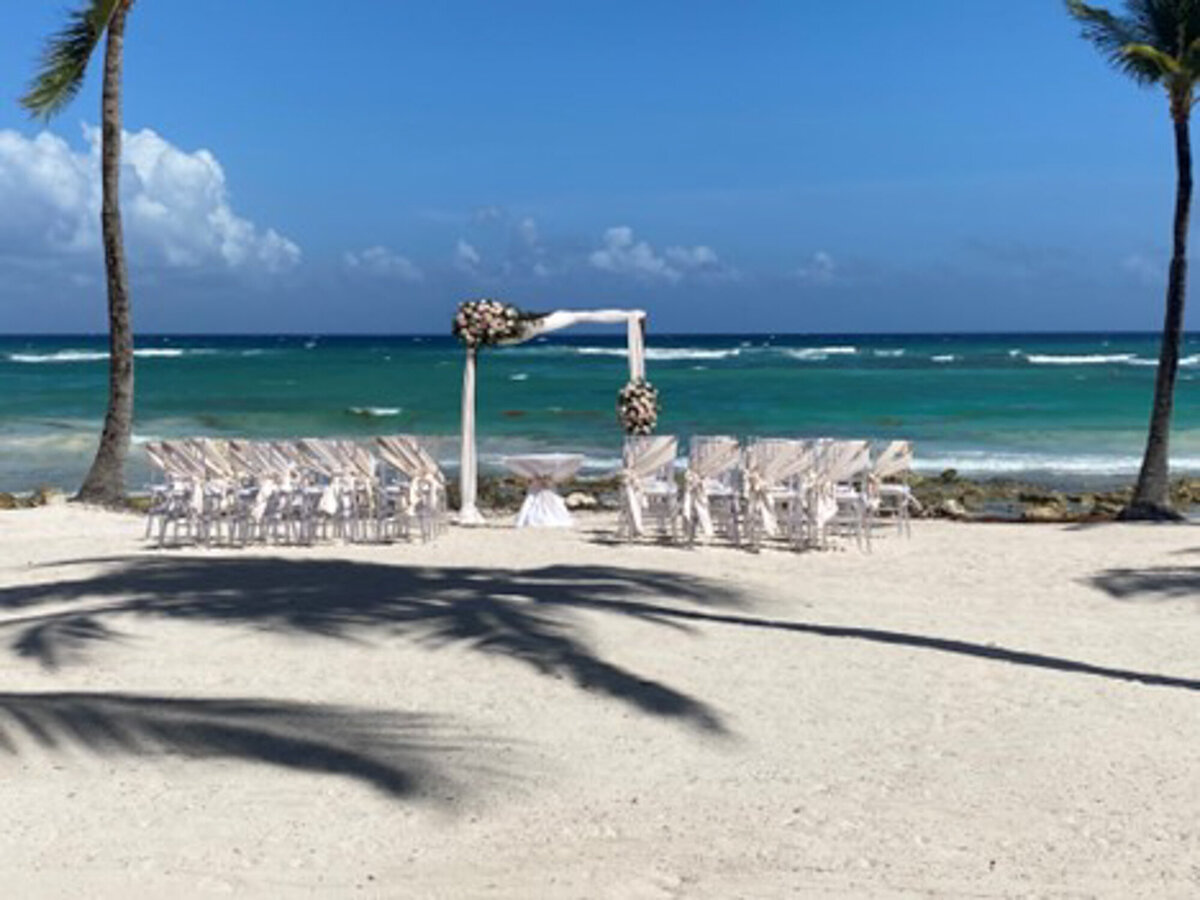 Beach wedding ceremony site with elegant florals and chairs at the seaside