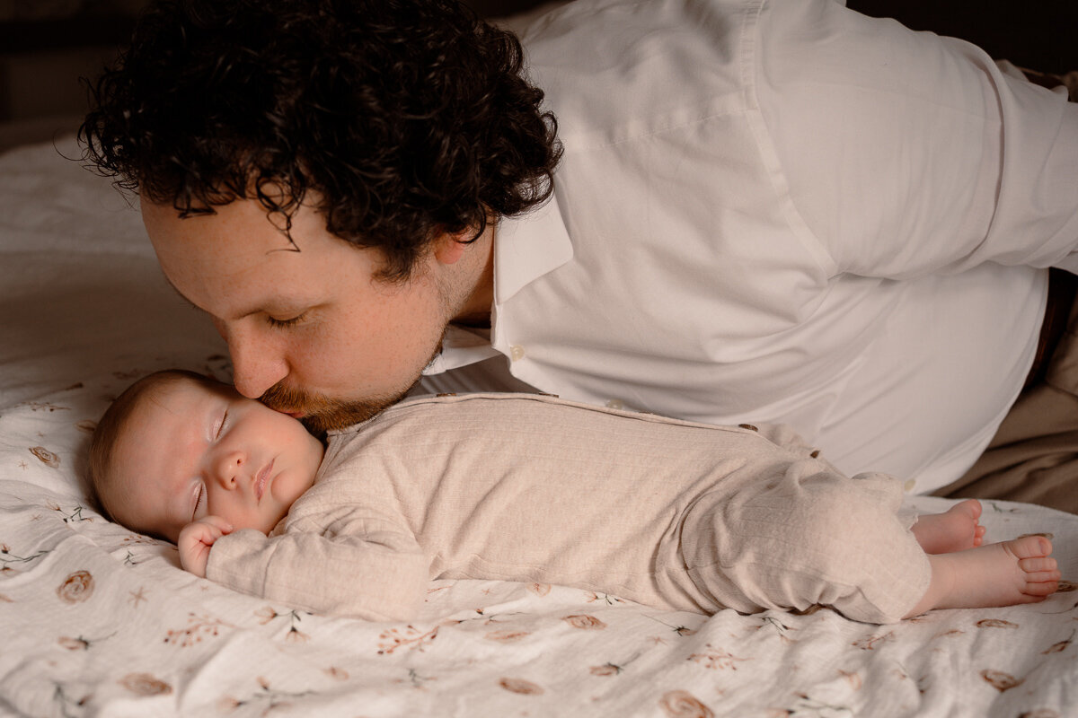 Vader geeft slapende newborn een kusje op zijn wang tijdens een newbornshoot