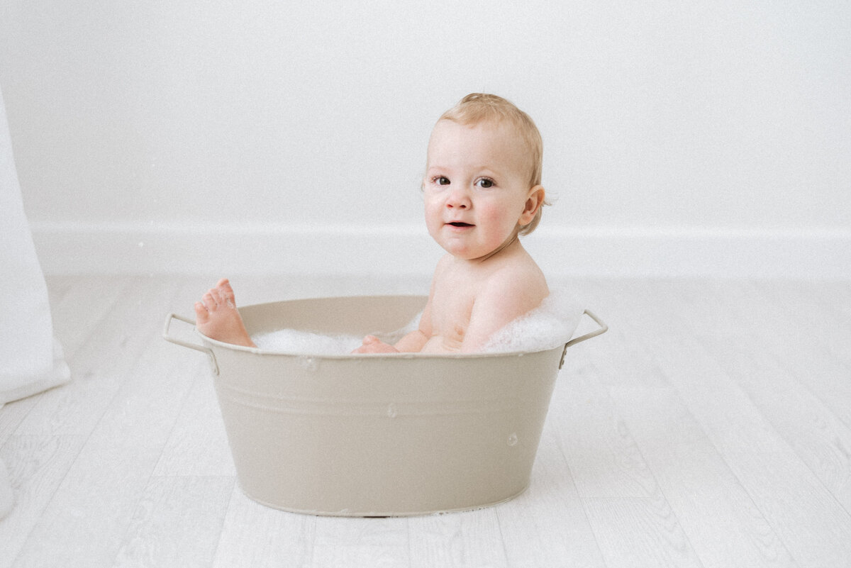 Baby laying in a bubble bath with feet poking out during cake smash photoshoot in west sussex