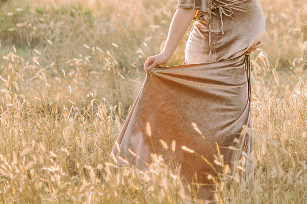 Woman in pink dress holding her baby bump in a field of yellow grass