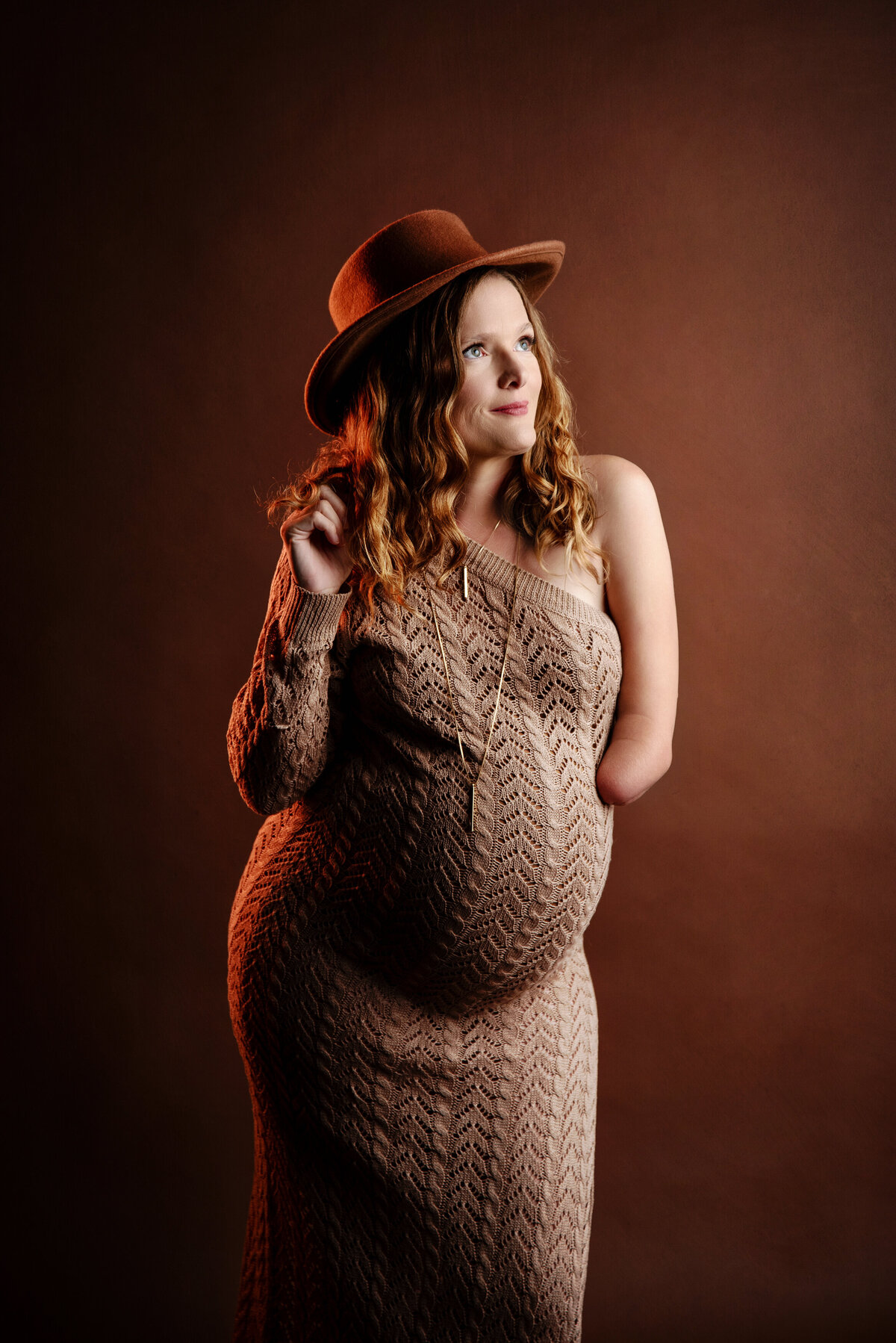 st-louis-maternity-photographer-pregant-mom-in-boho-style-knit-dress-and-hat-with-brown-background