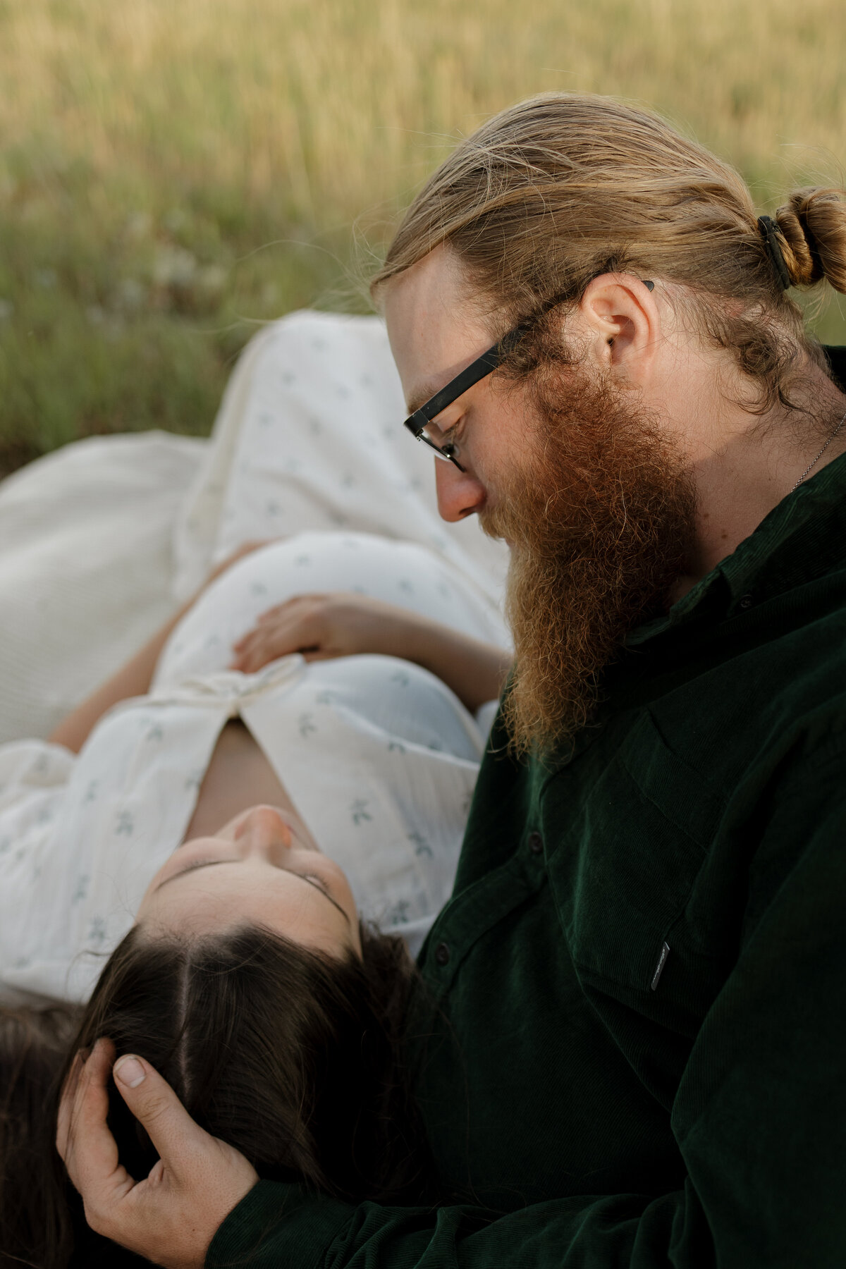 Expectant father looking down at partner while gently running hands through hair while mom is holding baby in belly