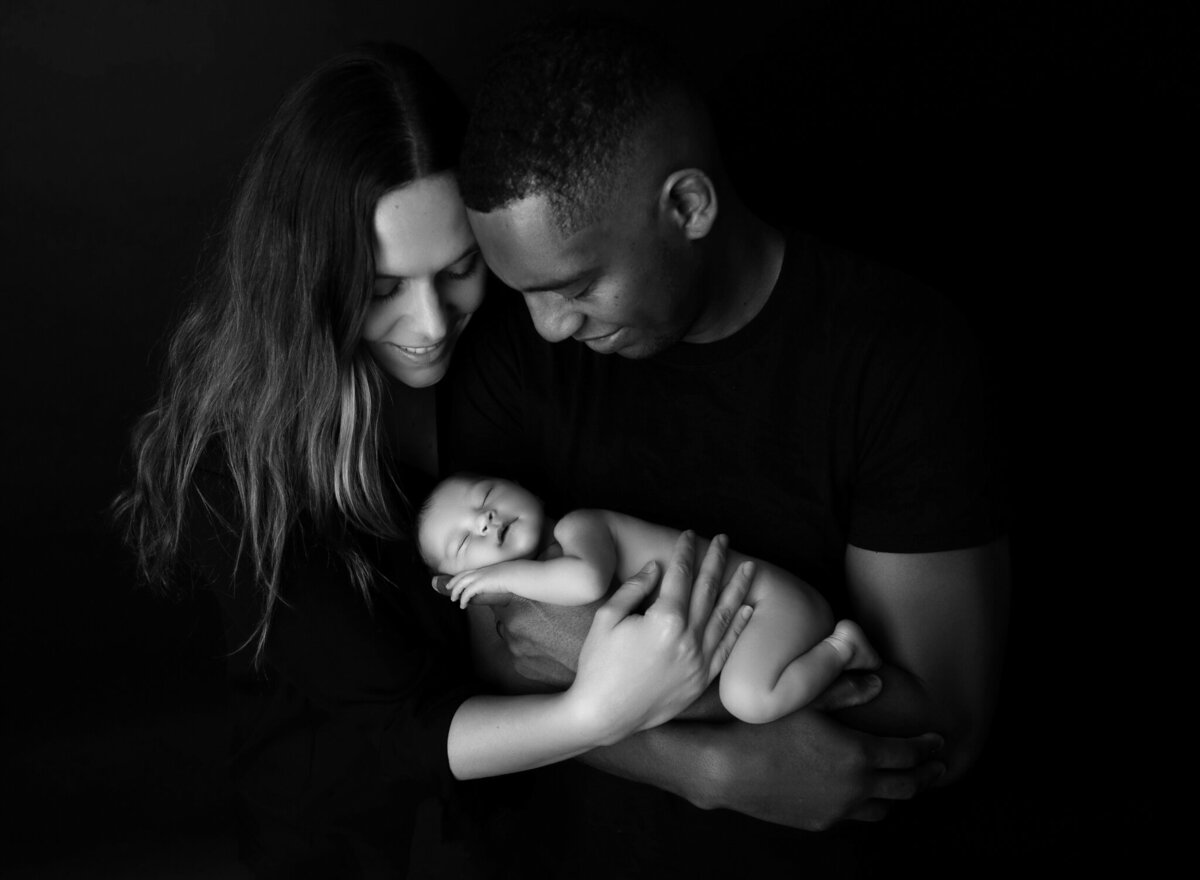Artistic black and white photo of parents cradling newborn baby with smiles and tender connection | Studio newborn photographer in Austin and Cedar Park