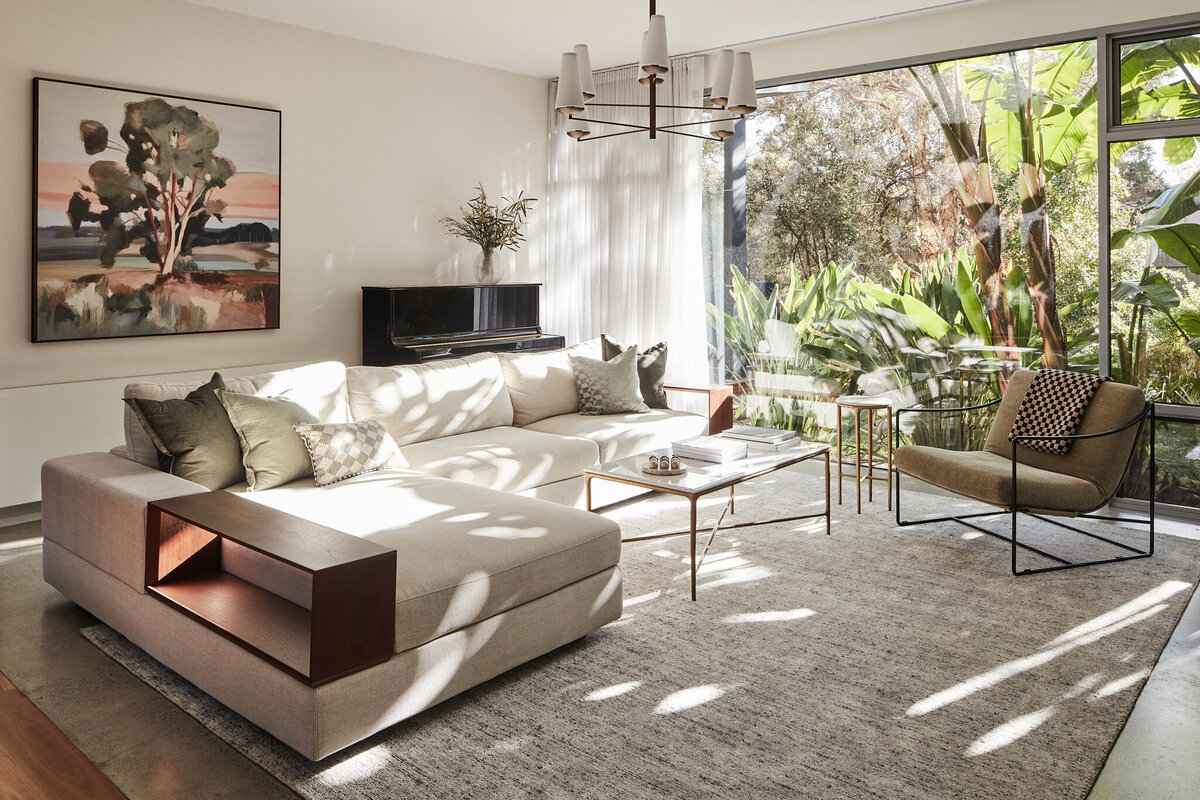 Brighton interior stylist living room with neutral sectional sofa, wall art, piano, and large glass windows overlooking garden.