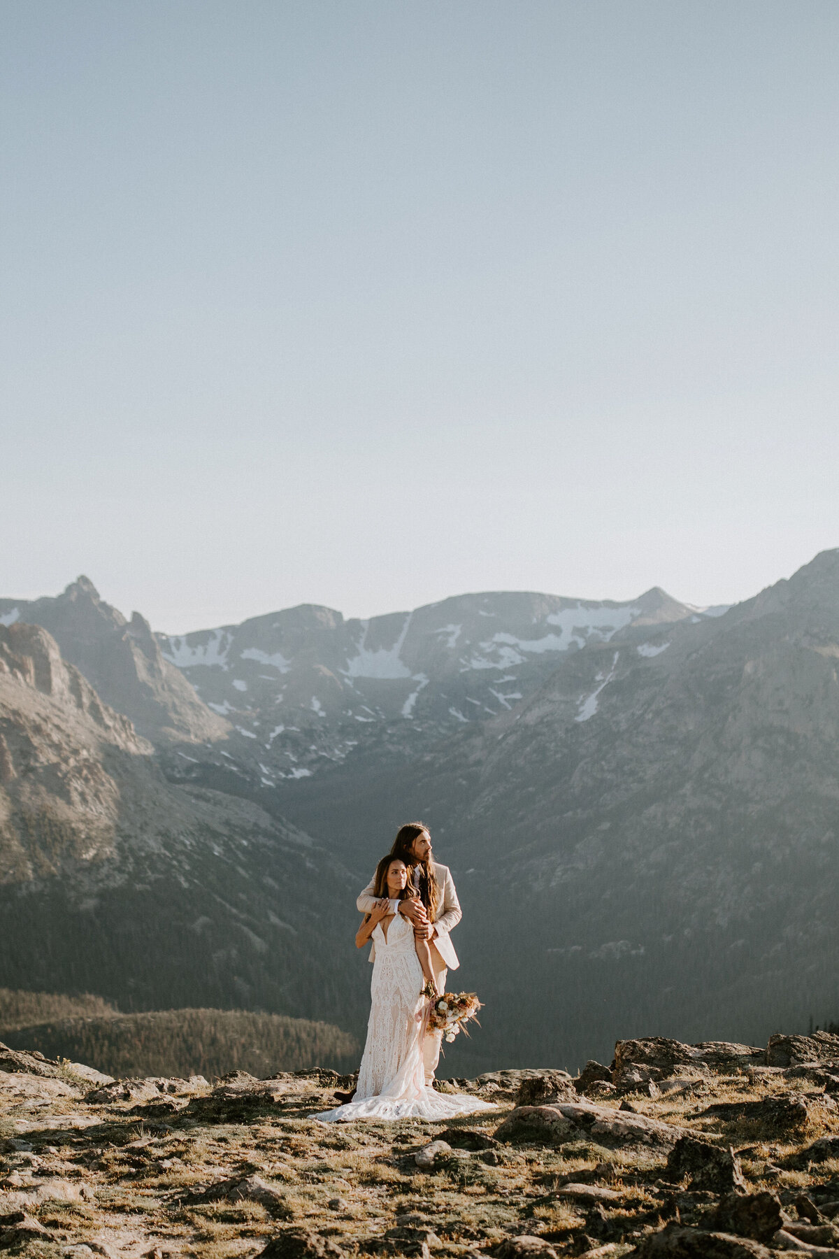 bride and groom wearing an ivory wedding gown and tuxedo pose in the mountains holding a bouquet