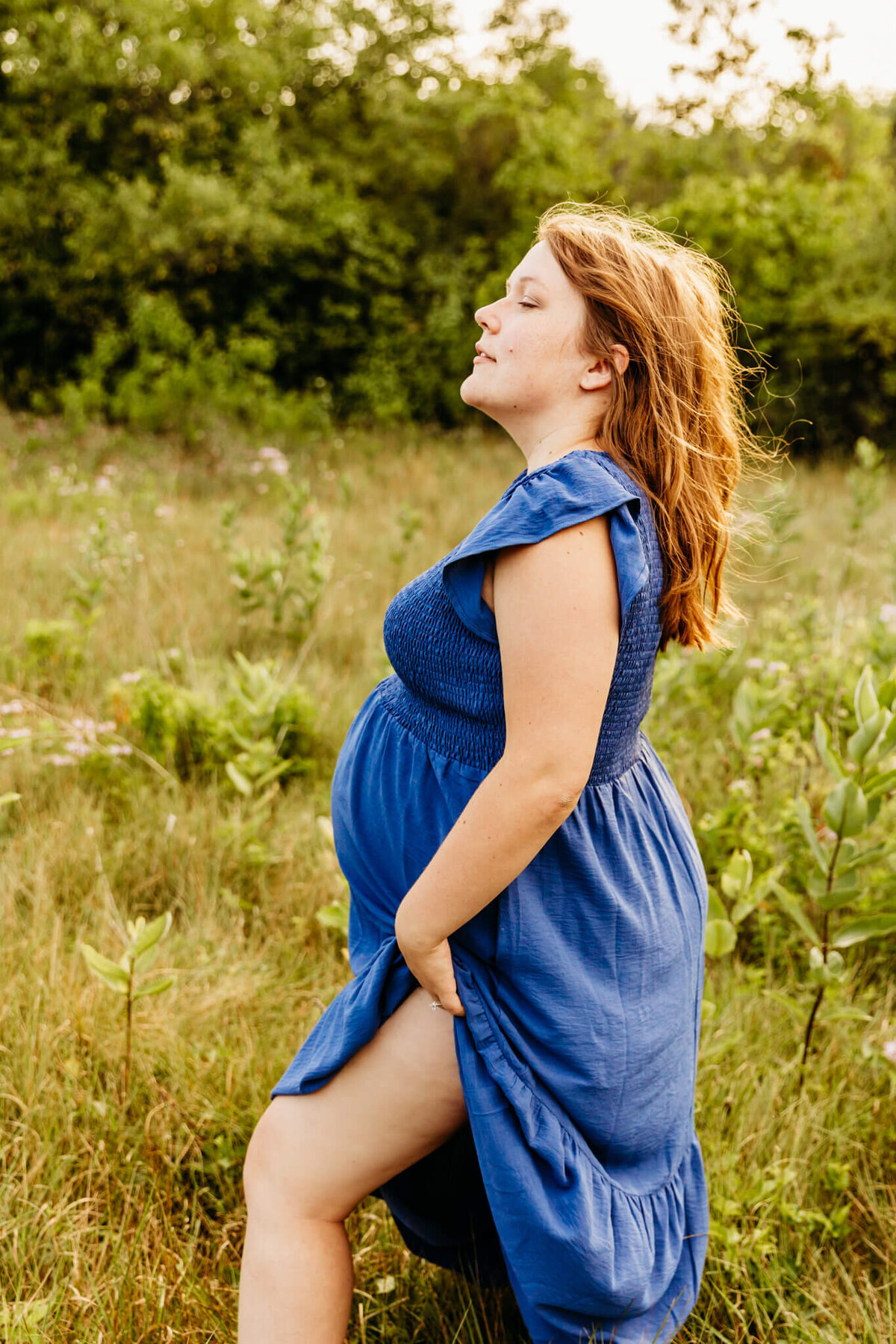 pregnant woman in a blue dress showing off her bump and leg by Ashley Kalbus Photography