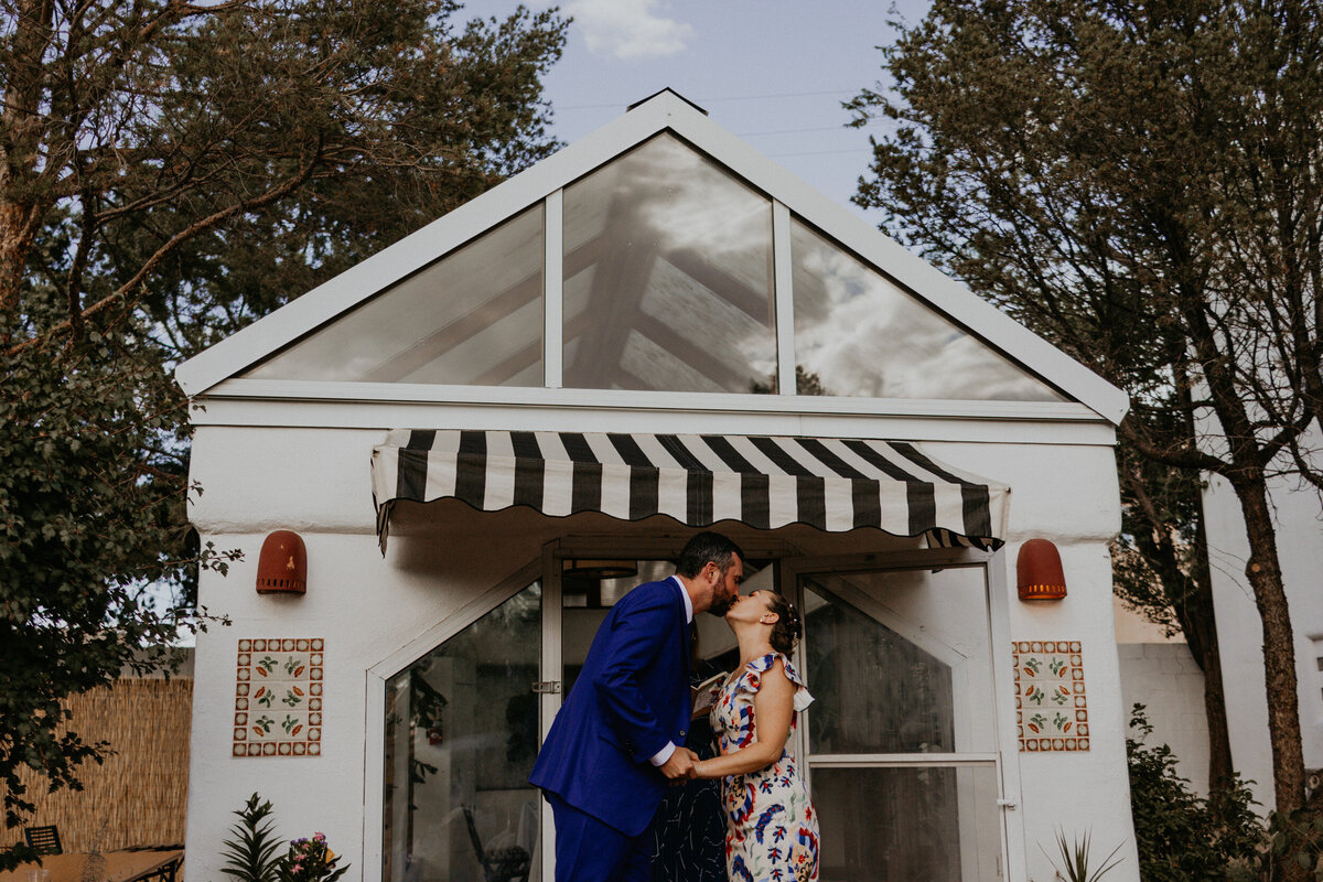 bride and grooms first kiss in front of a greenhouse