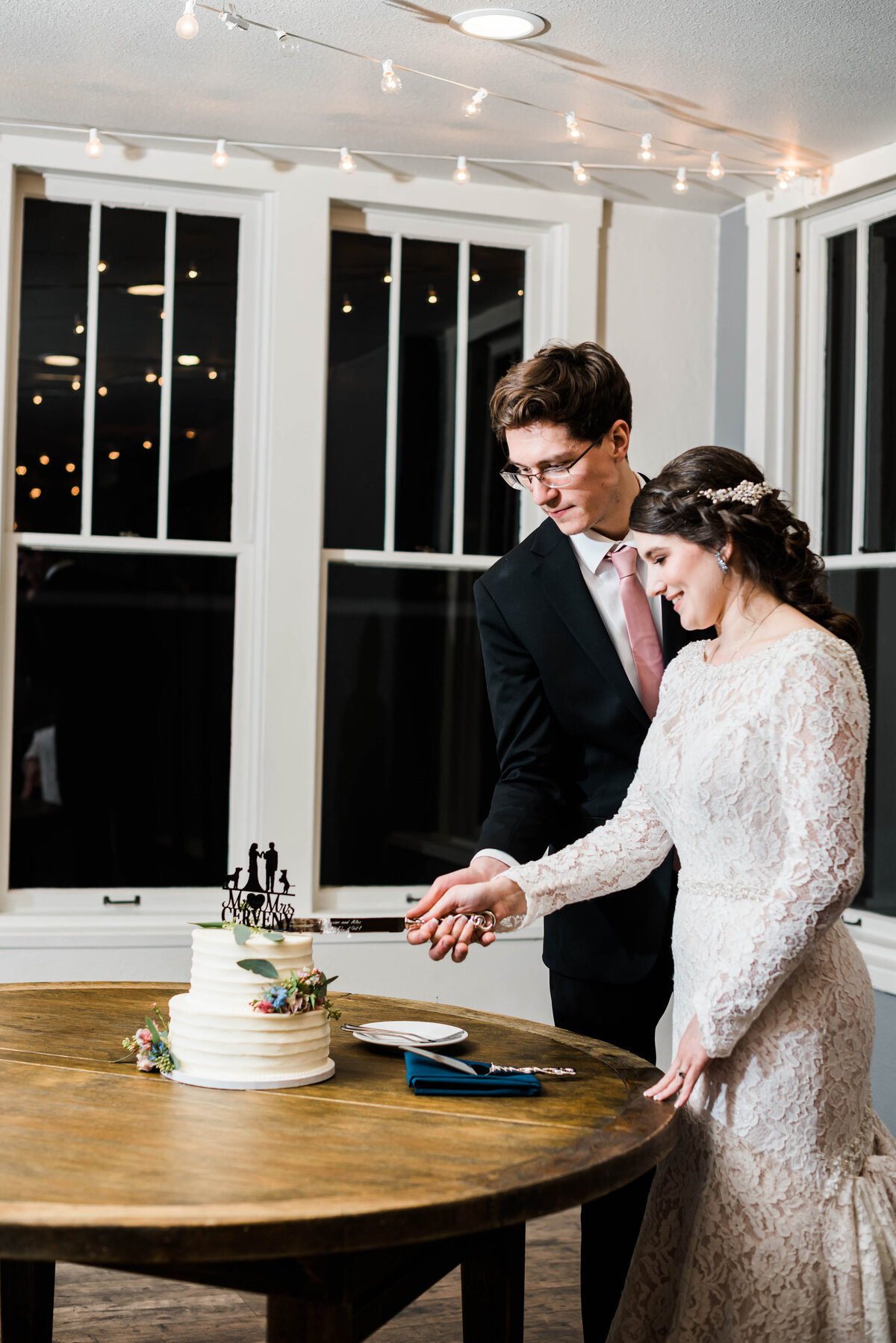 Denver wedding photographer captures bride and groom cutting into their cake together while both smile and hold the knife together