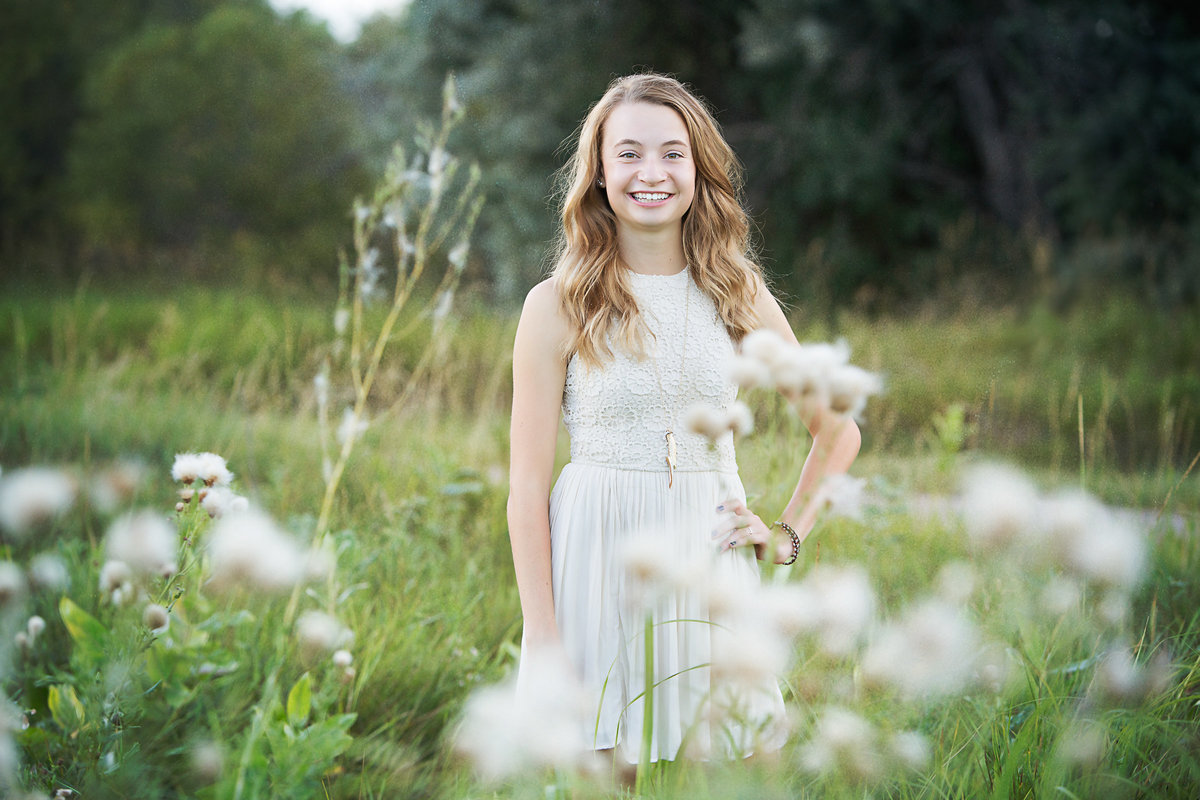 Beautiful senior girl in a cream dress in a field of fluffy grass