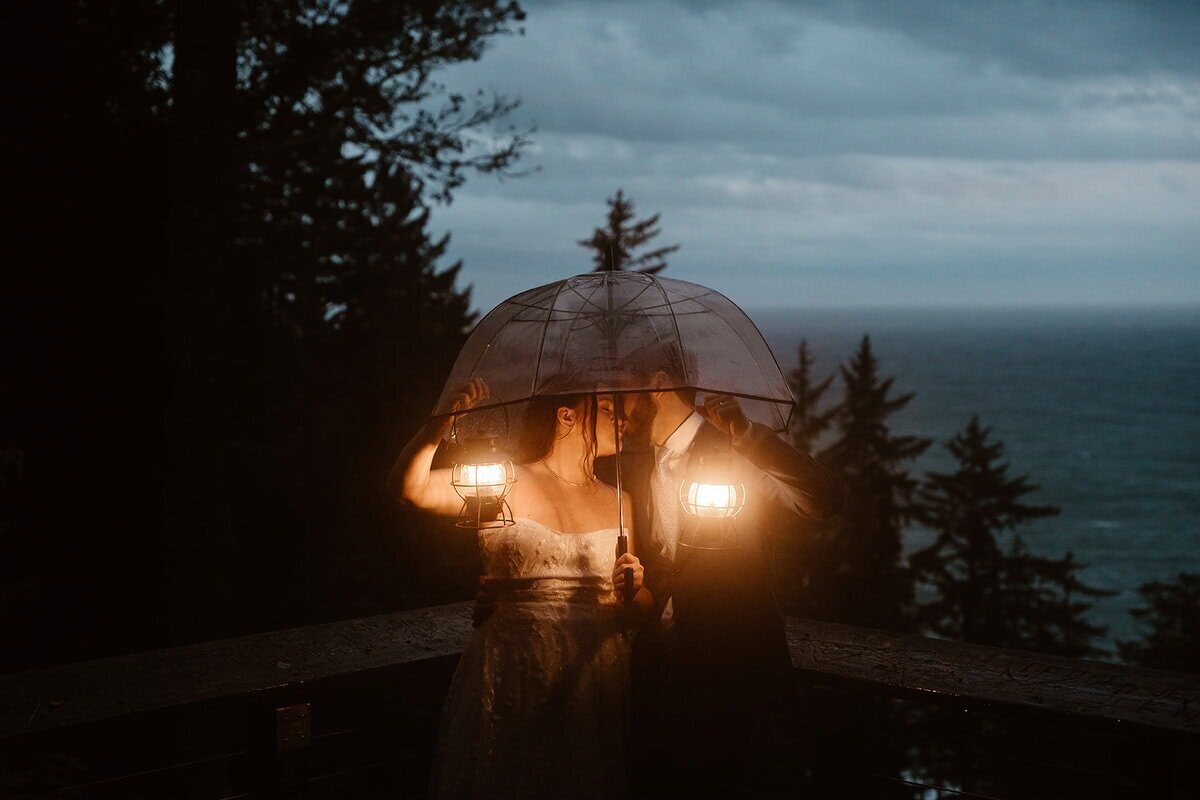 Couple holding lanterns while walking through cracked desert ground under a cloudy night sky with the moon glowing above distant mountains.