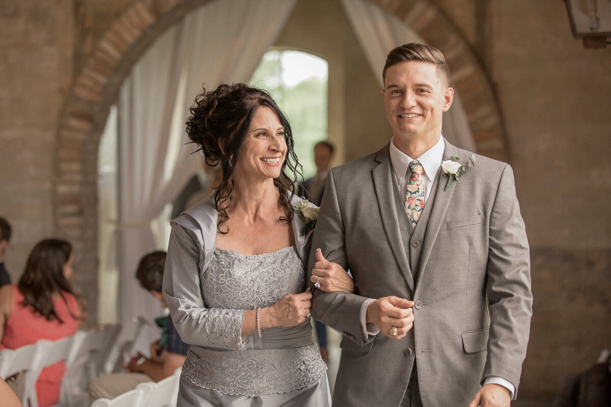 The groom escorts his mother down the aisle before assuming his place at the alter