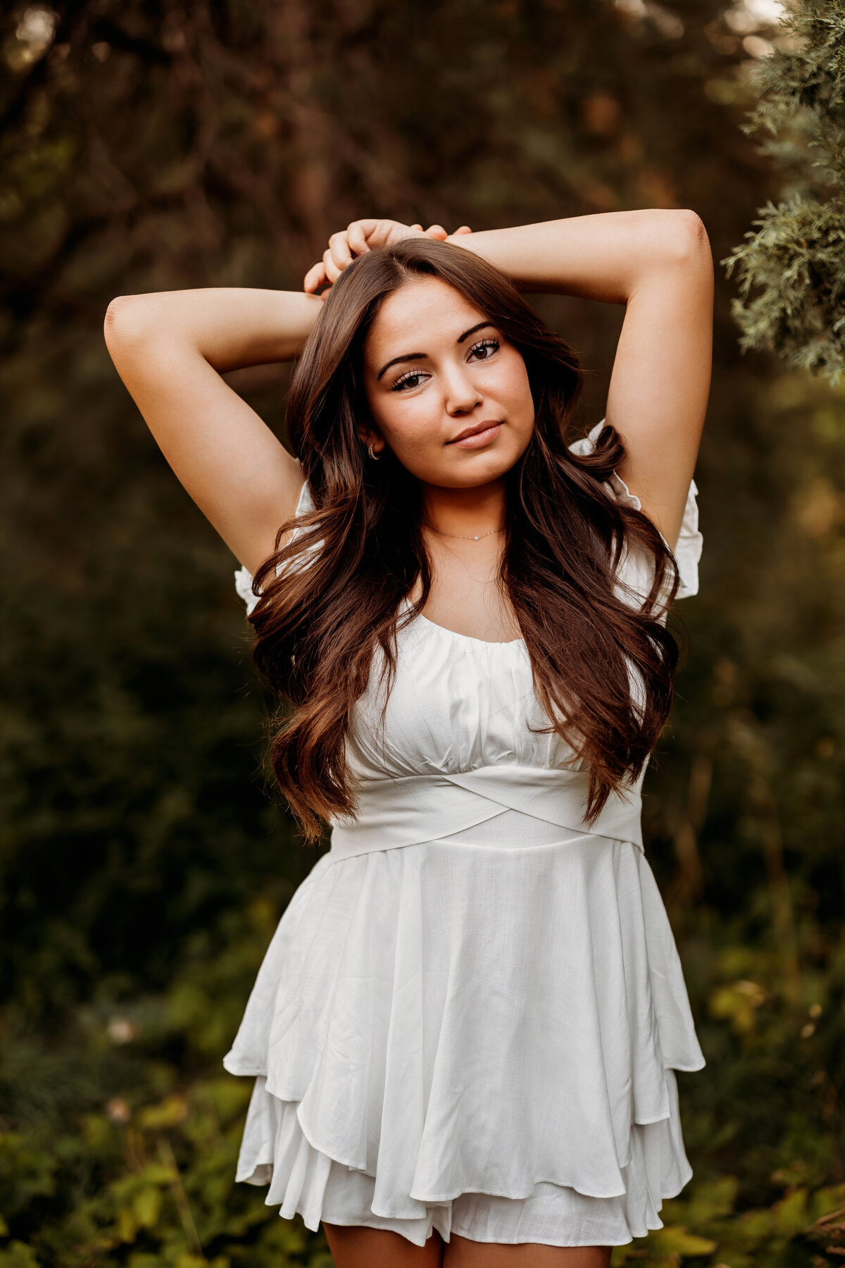High school teenage girl poses with her hands above her head in a white dress