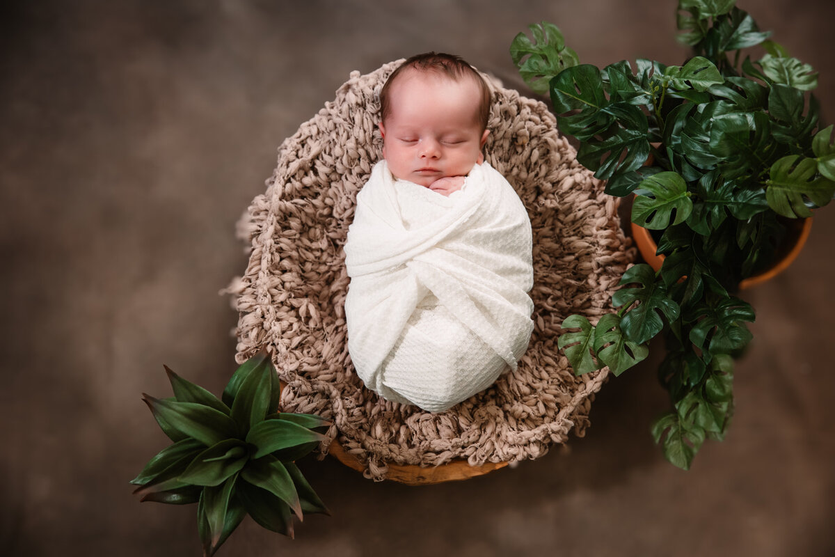 A newborn baby sleeps in the studio of a Milwaukee Newborn Photographer in a wooden basket and white swaddle