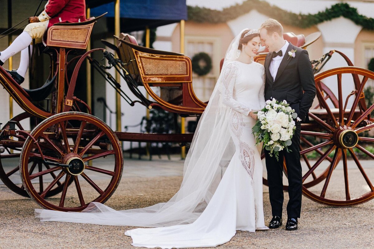 Newlyweds sharing a kiss beside a horse-drawn carriage.
