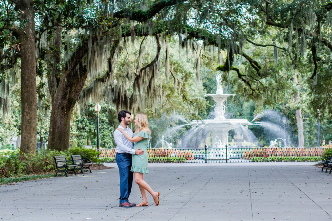 A couple stands in front of a fountain while embracing each other.