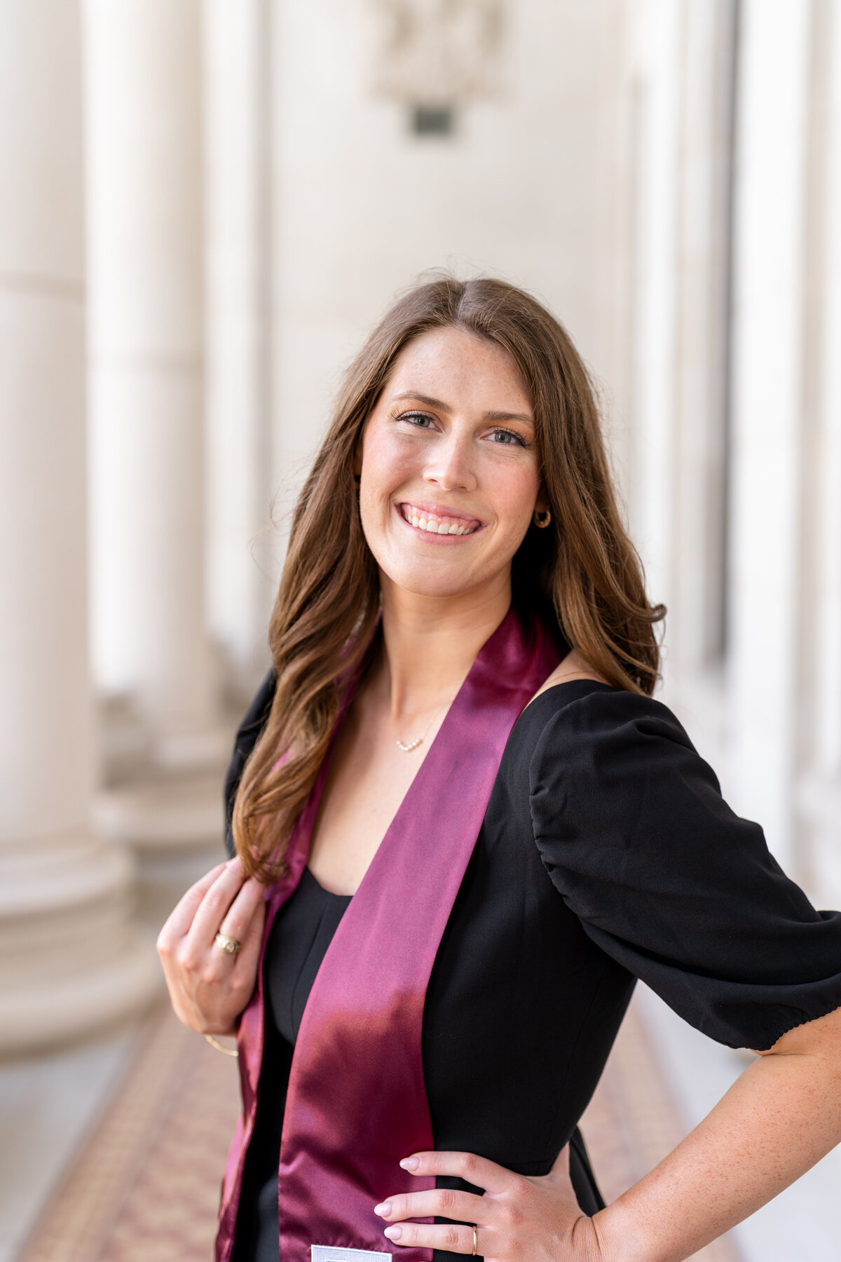 Texas A&M senior girl smiling with hand on hip and other hand touching hair while wearing black dress and Aggie stole in columns of Administration Building