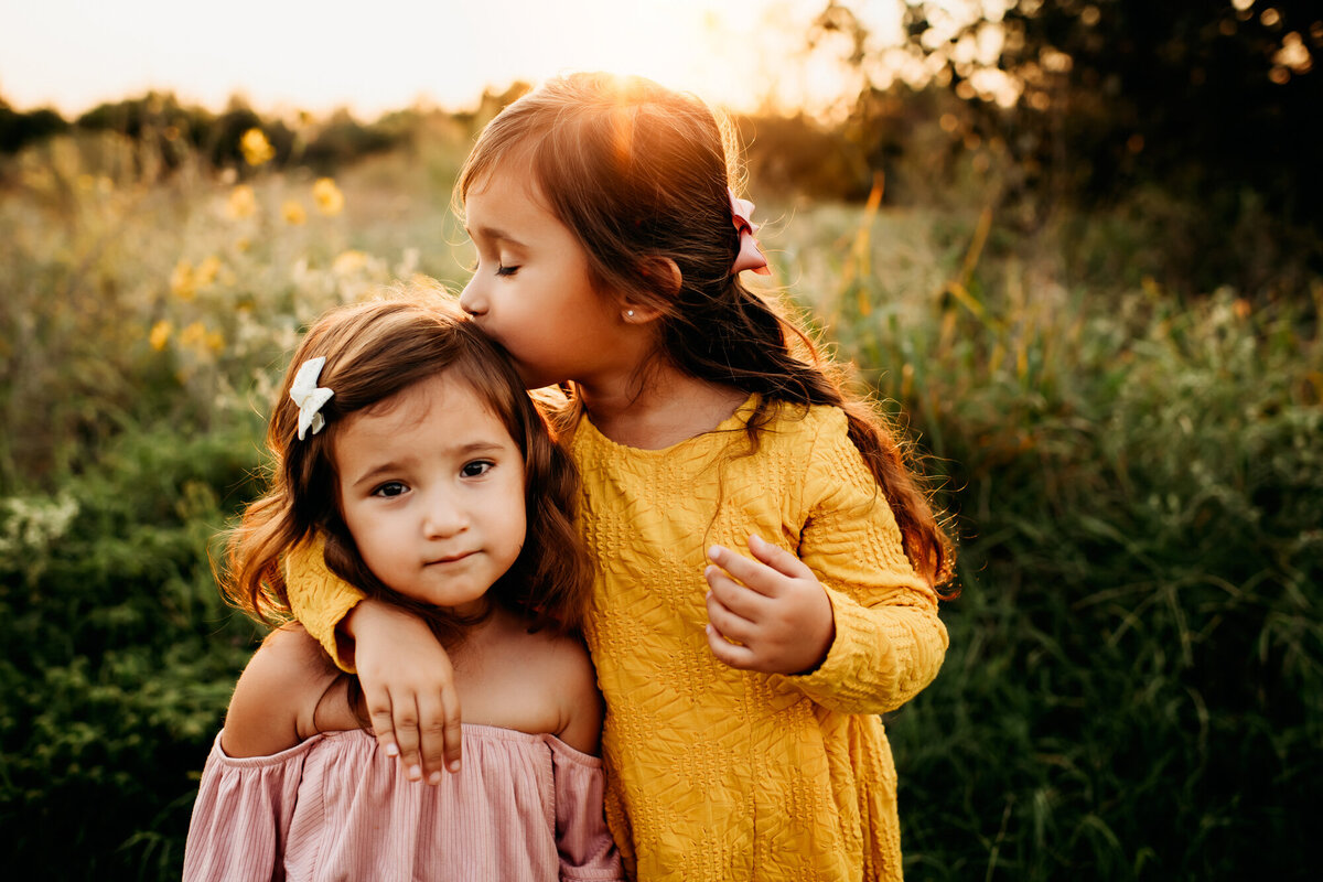 Family Photographer. an older sister kisses her younger sister outside