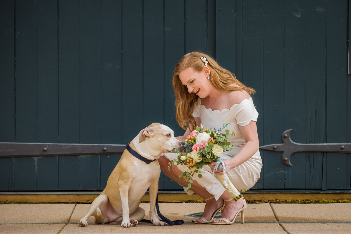 Bride bending down to show her bouquet to her dog at Phoenixville Foundry, captured by Fox & Brazen for fun and creative wedding photography.