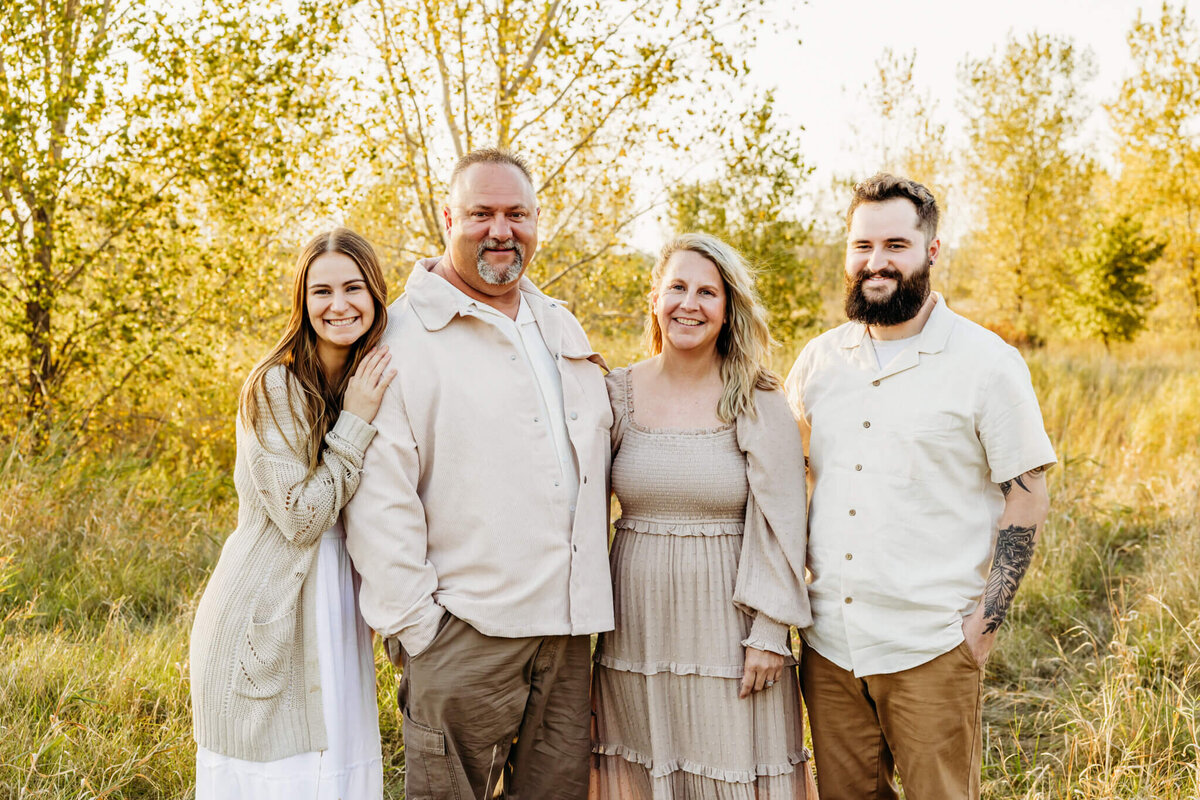 beautiful image of a mother and father smiling as they stand with their adult children in a field near Milwaukee.